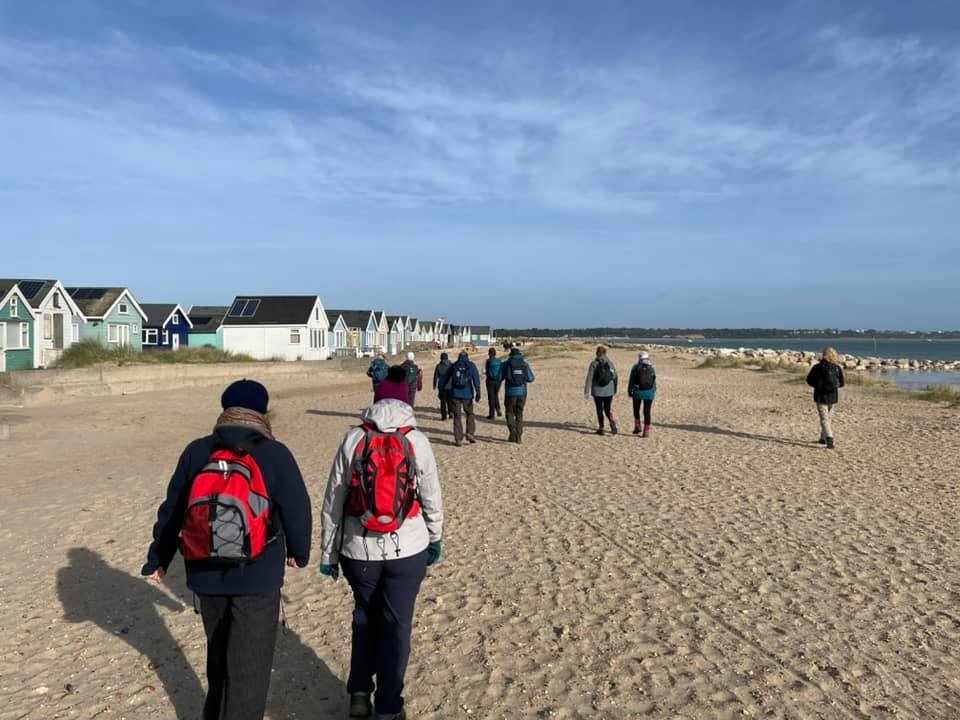 Group of people walking on a sandy beach near colorful beach huts on a clear day.