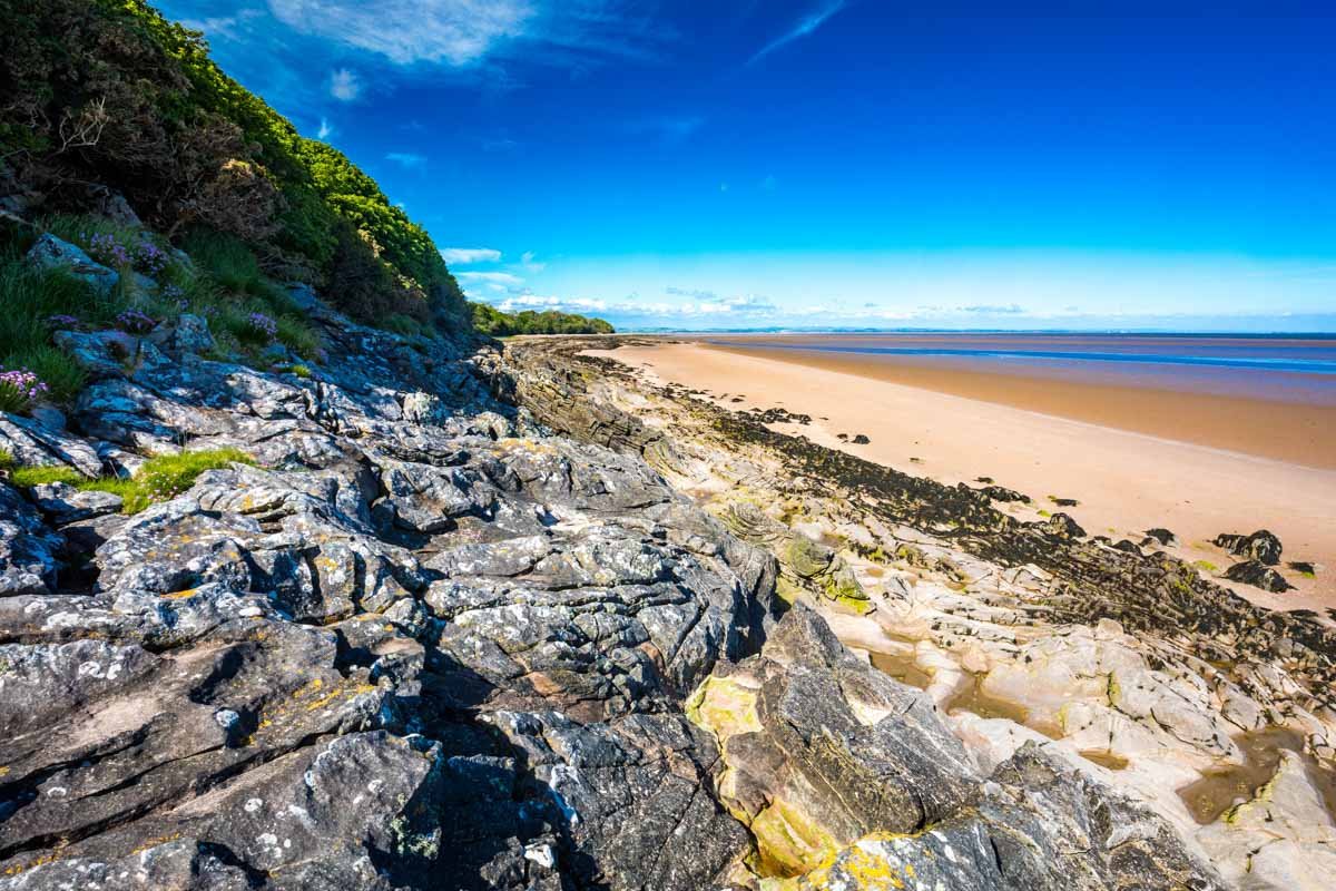 Rocky beach with sandy shore, lush green trees under blue sky