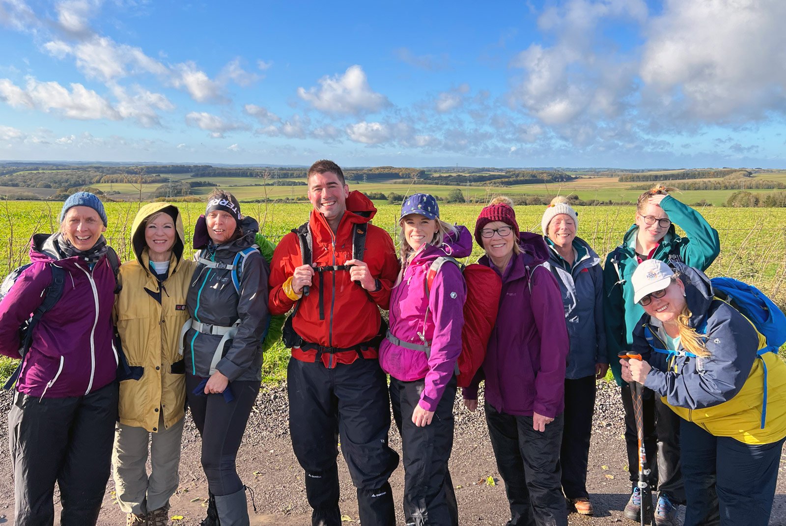 Group of people in hiking gear posing outdoors with a scenic countryside background.