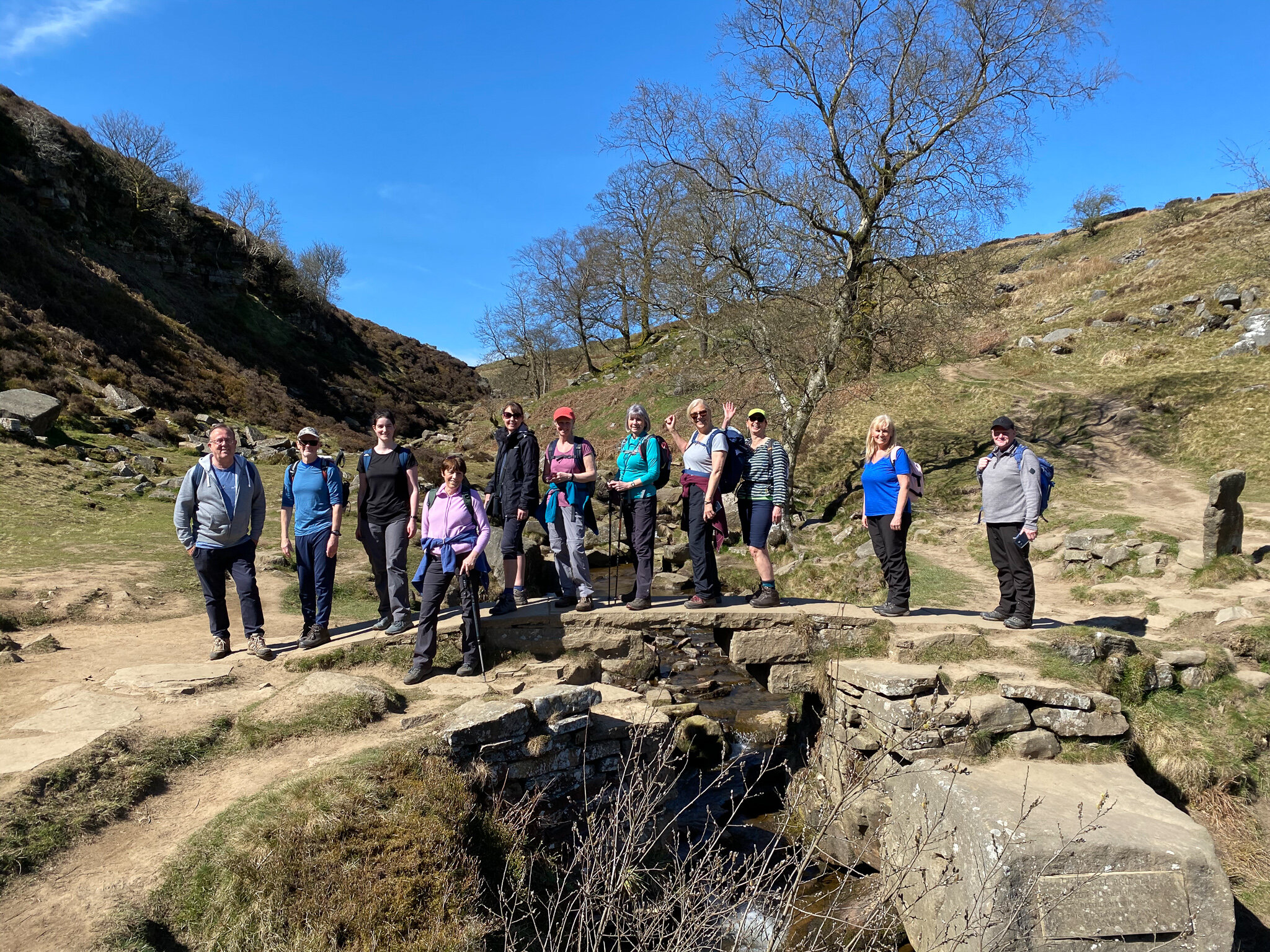 A group of people standing on a stone footbridge in a rural landscape during a sunny day.