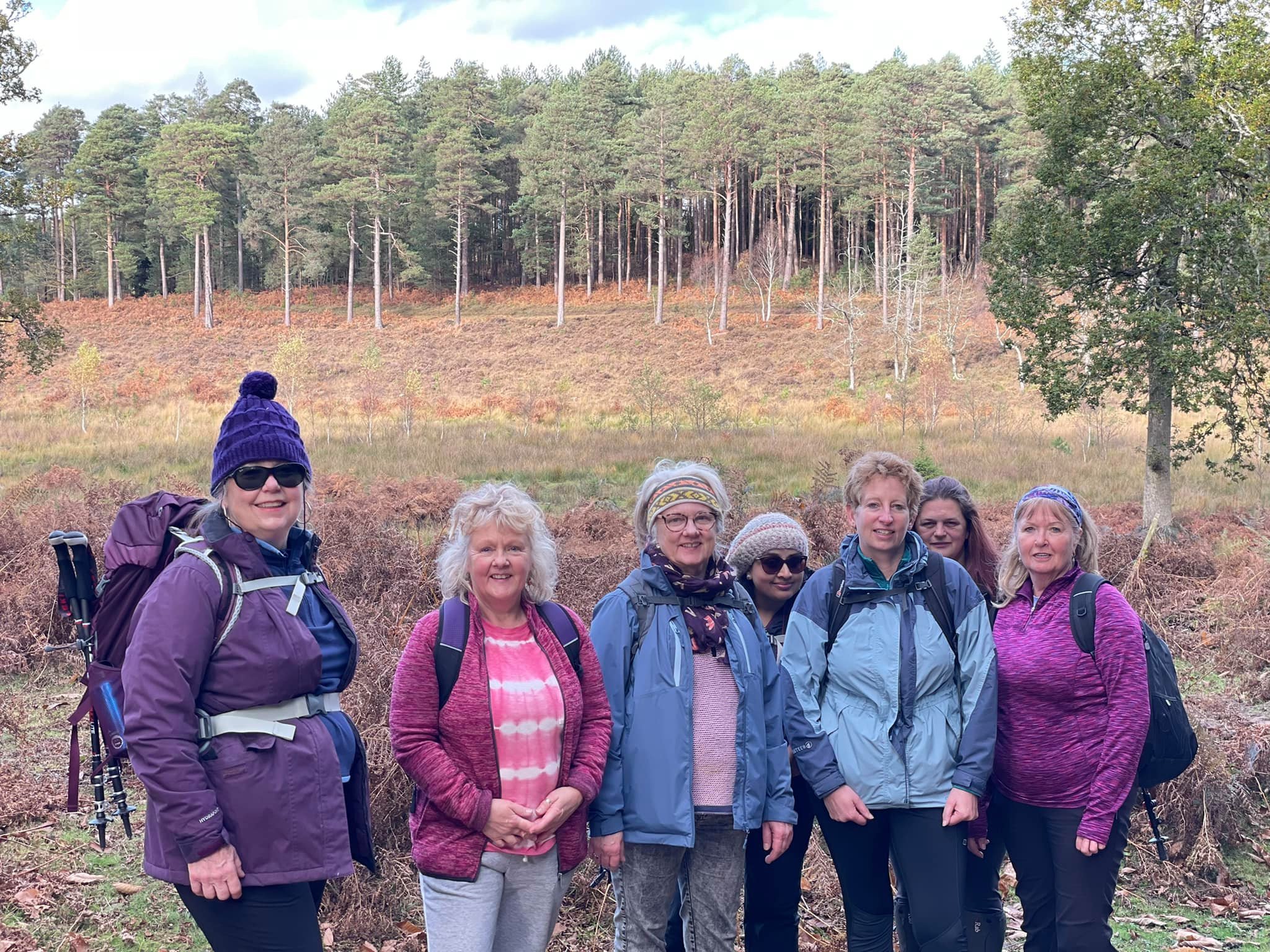 Group of women hiking in a forested area with autumn foliage, wearing jackets and backpacks.