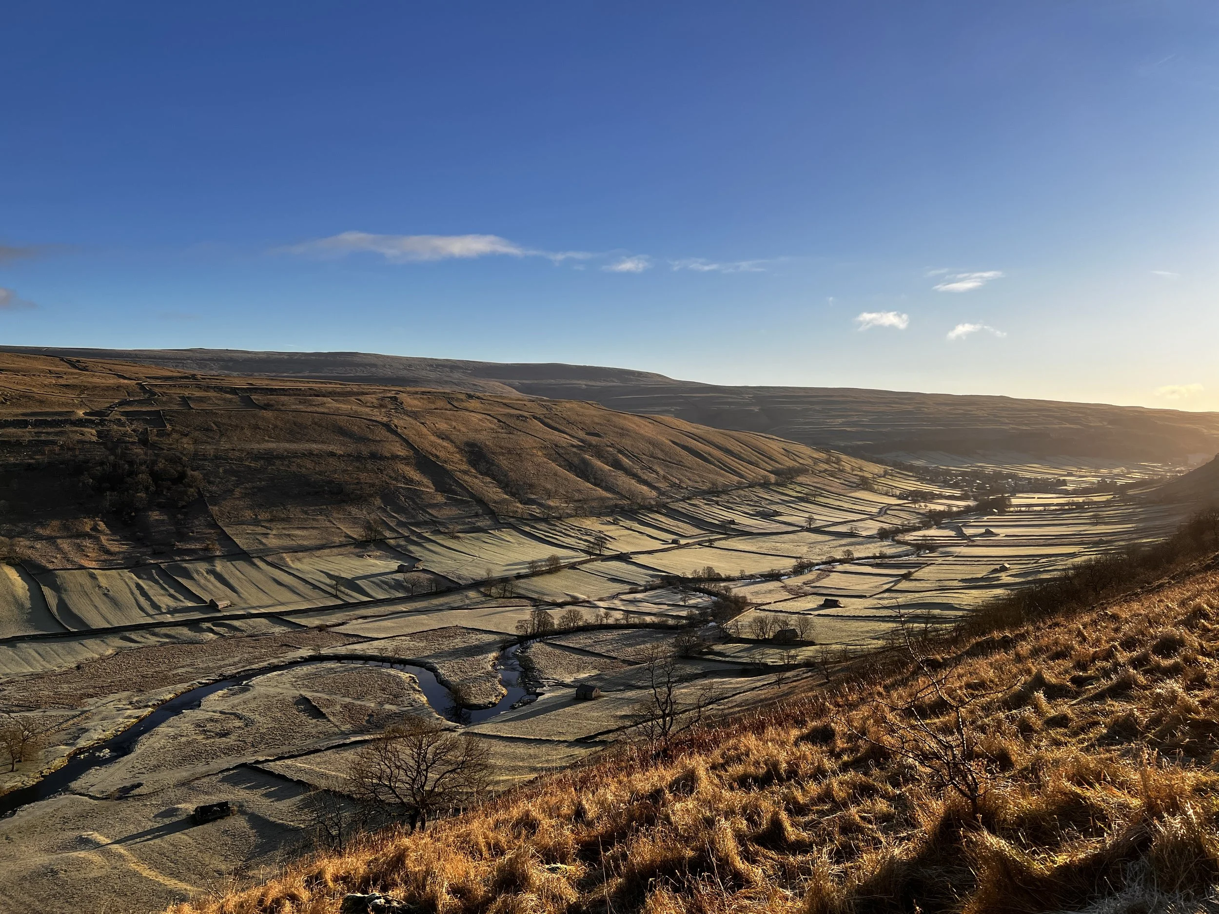 A scenic landscape featuring terraced farming fields on rolling hills with brown and green hues under a clear blue sky.
