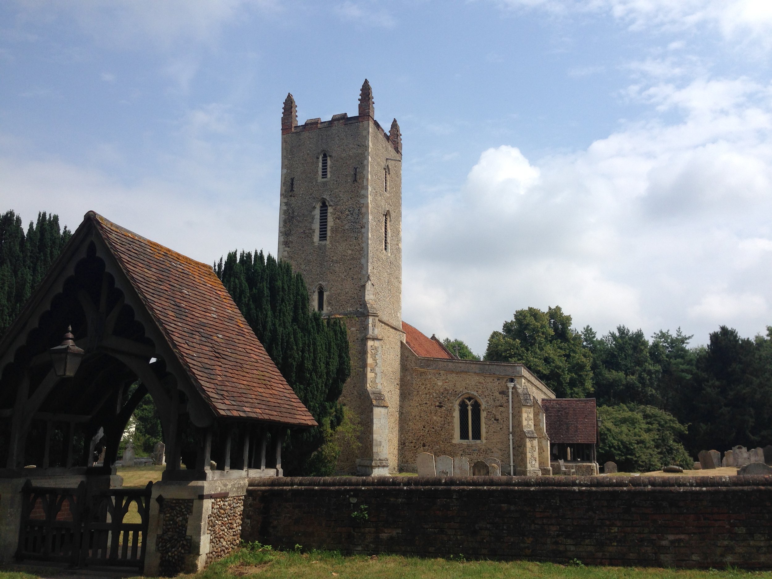 Historic stone church with a tall tower, arched windows, and surrounding graveyard, set in a rural landscape against a partly cloudy sky.