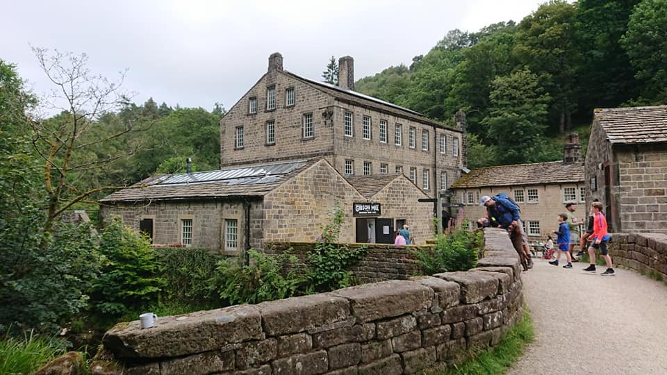 Historic stone buildings surrounded by greenery, with people walking and exploring a cobblestone path.