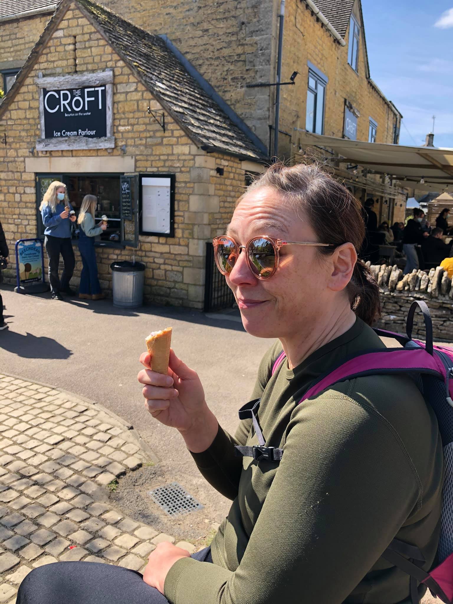 Person holding an ice cream cone outside The Croft Ice Cream Parlour, with a stone building and cobblestone path visible.
