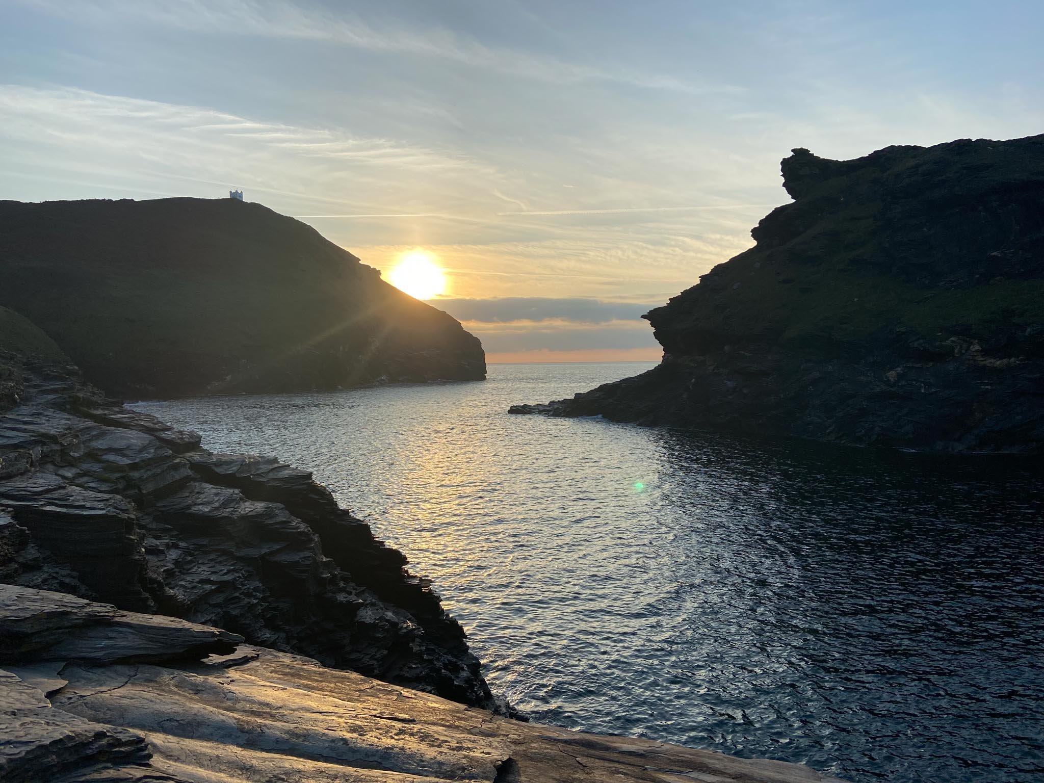 Sunset over a rocky coastal landscape with a silhouette of cliffs and a calm sea.