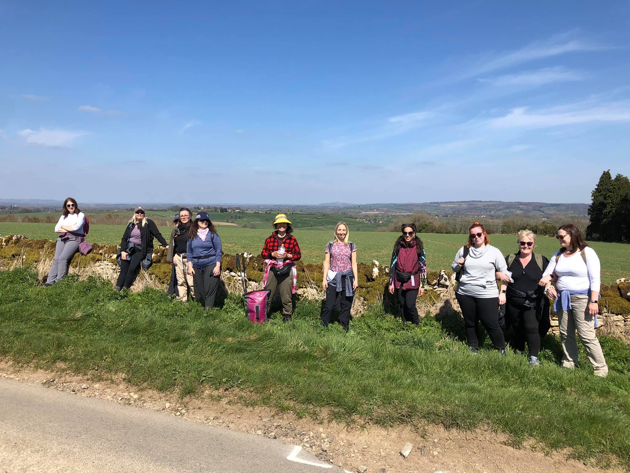 Group of people standing in front of a stone wall with a scenic countryside view and blue sky