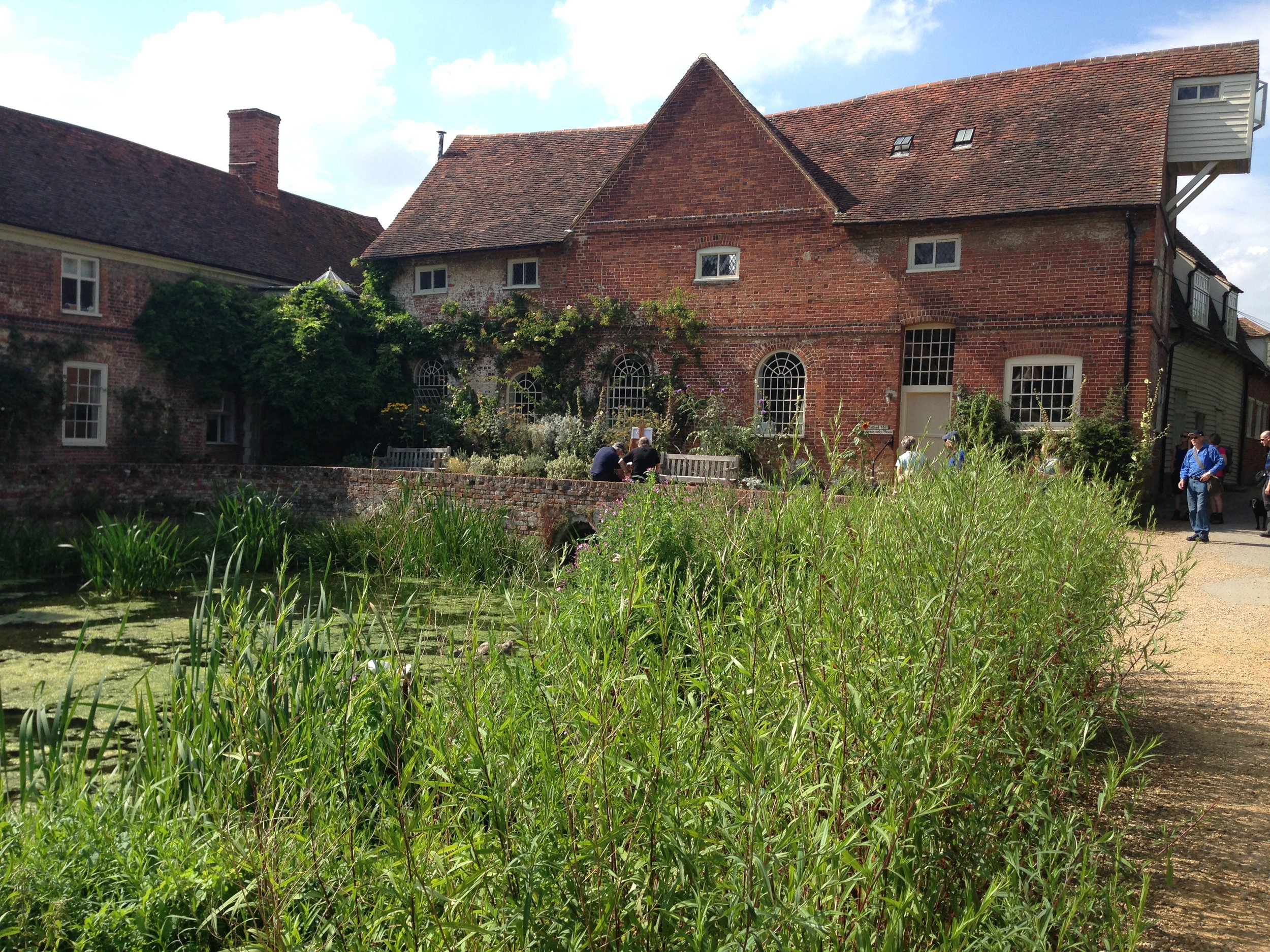 Historic brick building with ivy, garden, and pond.