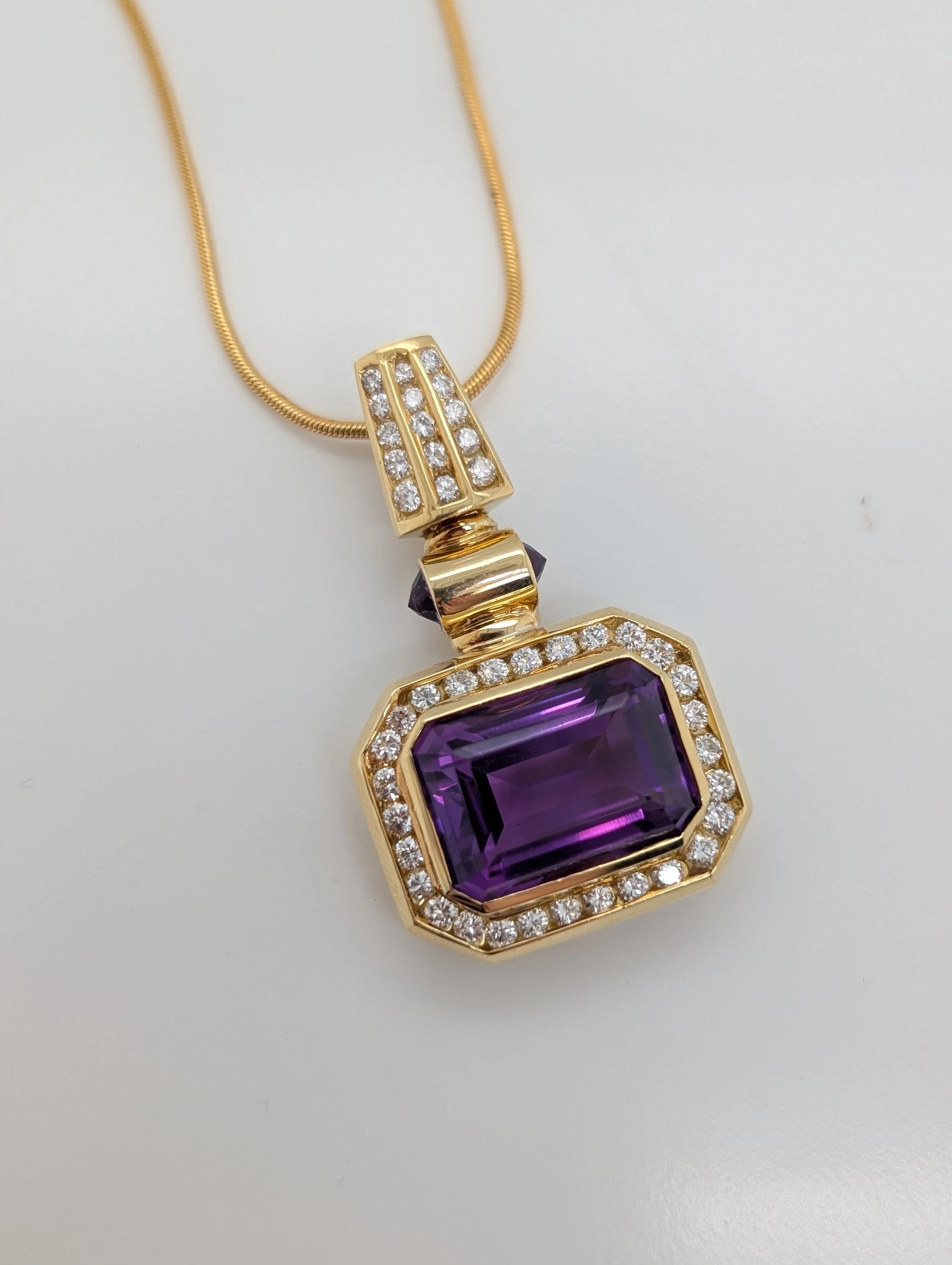 18k yellow gold emerald cut amethyst and diamond halo pendant with amethysts and diamonds on the snap bail (230-1695). Pendant is shown on a 14k yellow gold 24inch snake chain (430-710)