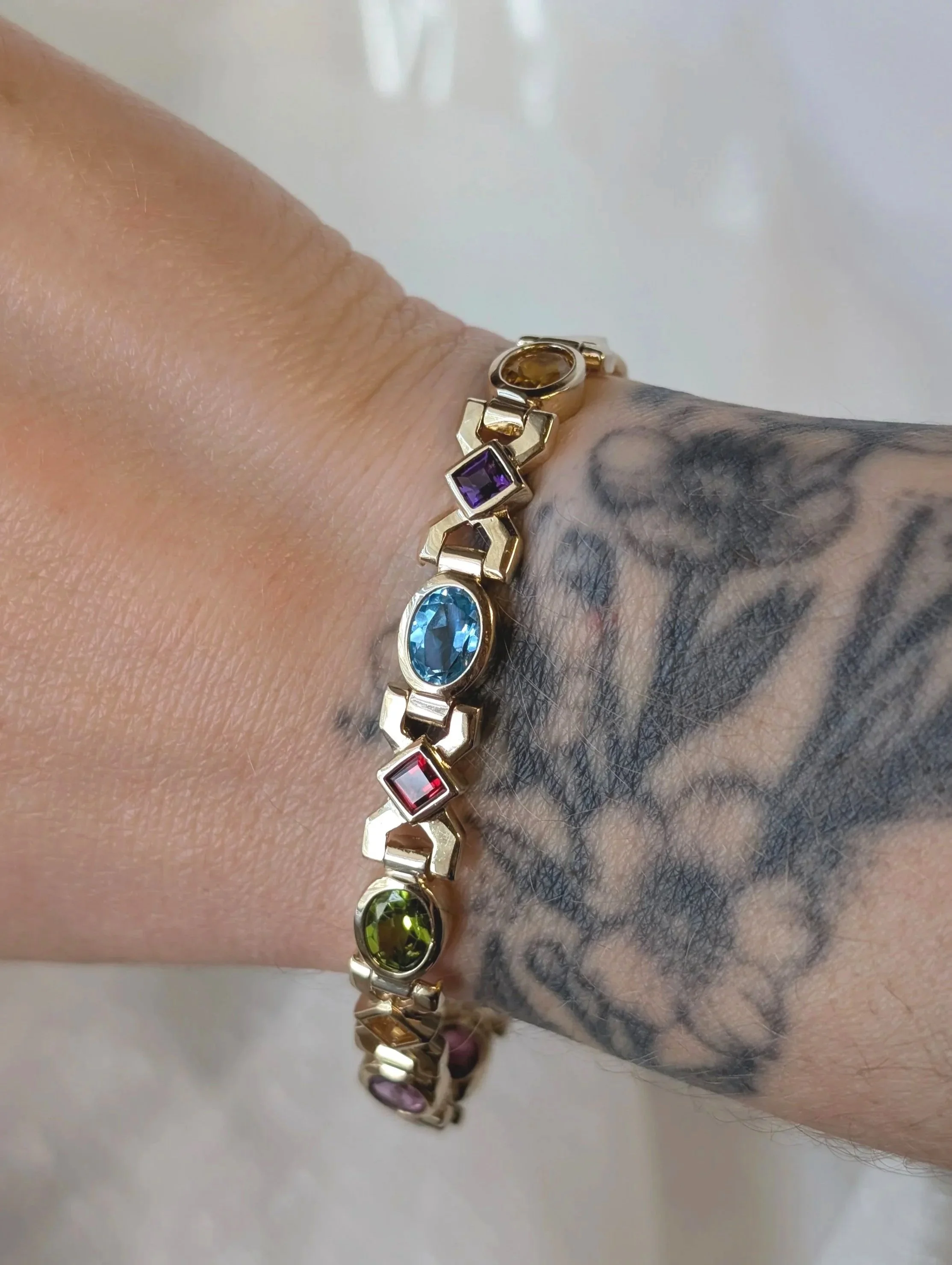 14k yellow gold multi-gemstone bracelet bezel set with amethyst, citrine, blue topaz, peridot, and garnet. (240-1182)