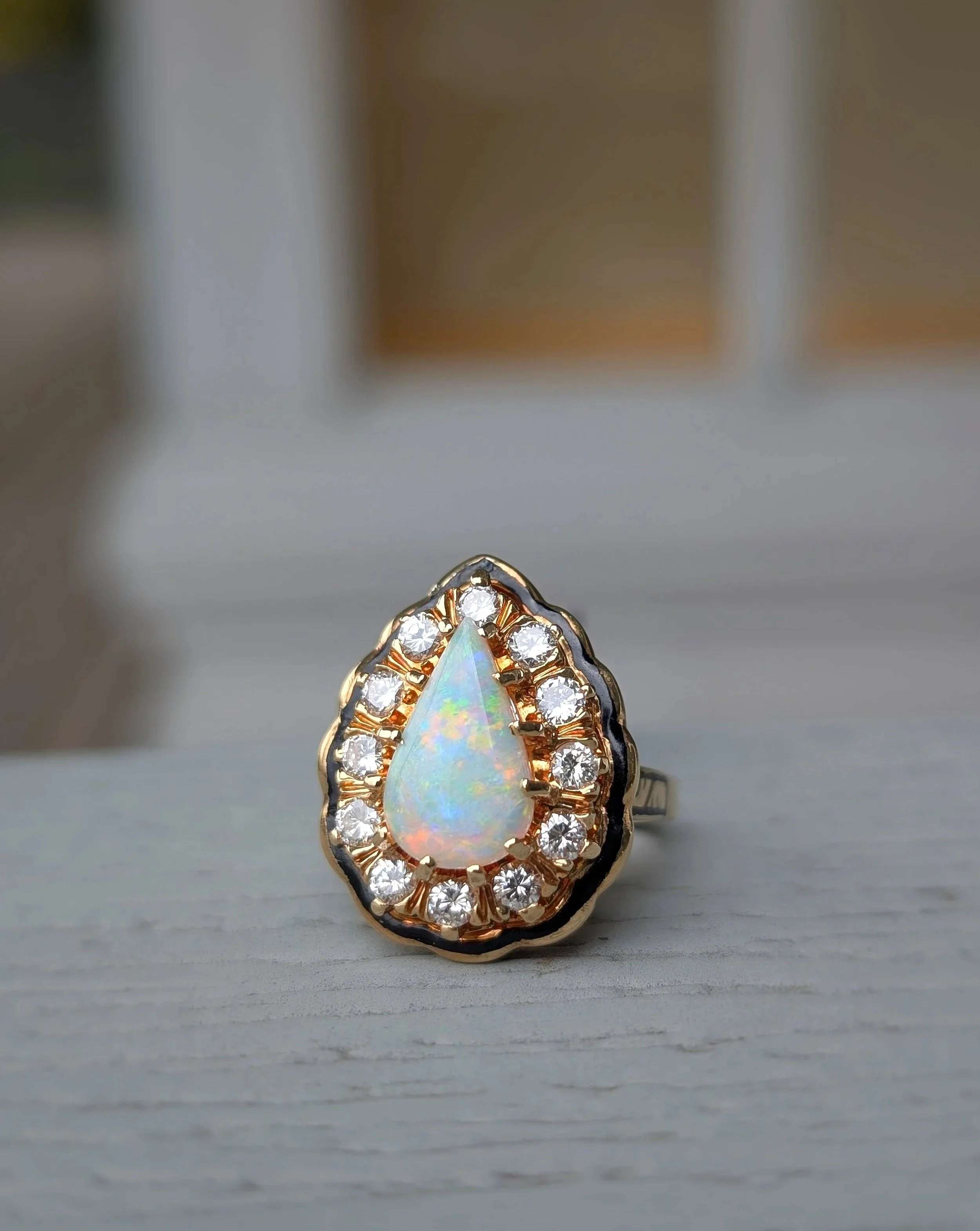 18k yellow gold pear shaped opal ring with a diamond and black enamel scalloped halo. Size 5.5. (200-2330)