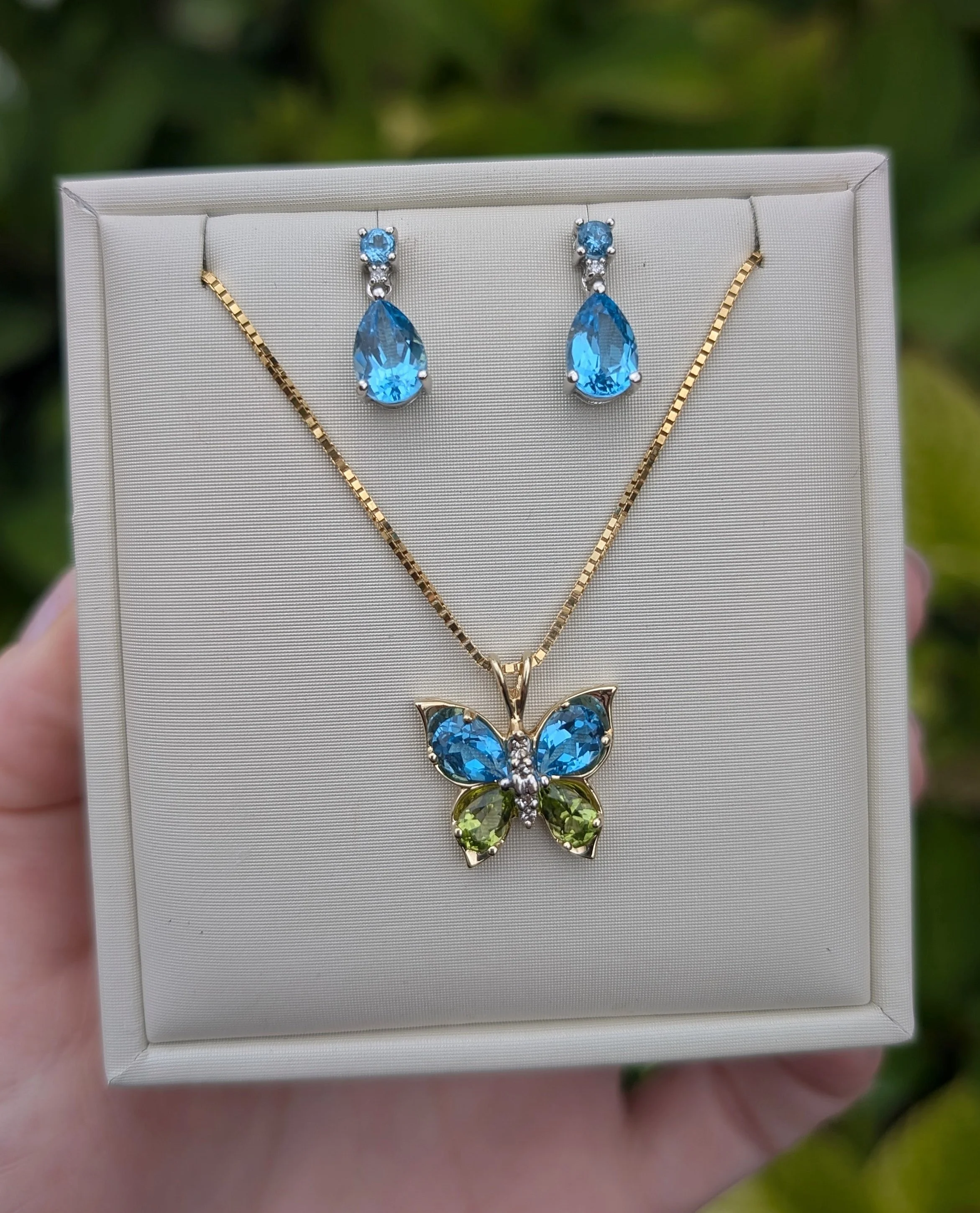 TOP: 14k white gold blue topaz and diamond dangle earrings with post and clutch closures. (210-3751)
BOTTOM: 14k yellow gold blue topaz, peridot, and diamond butterfly pendant on a 14k yellow gold box chain. (230-1762)