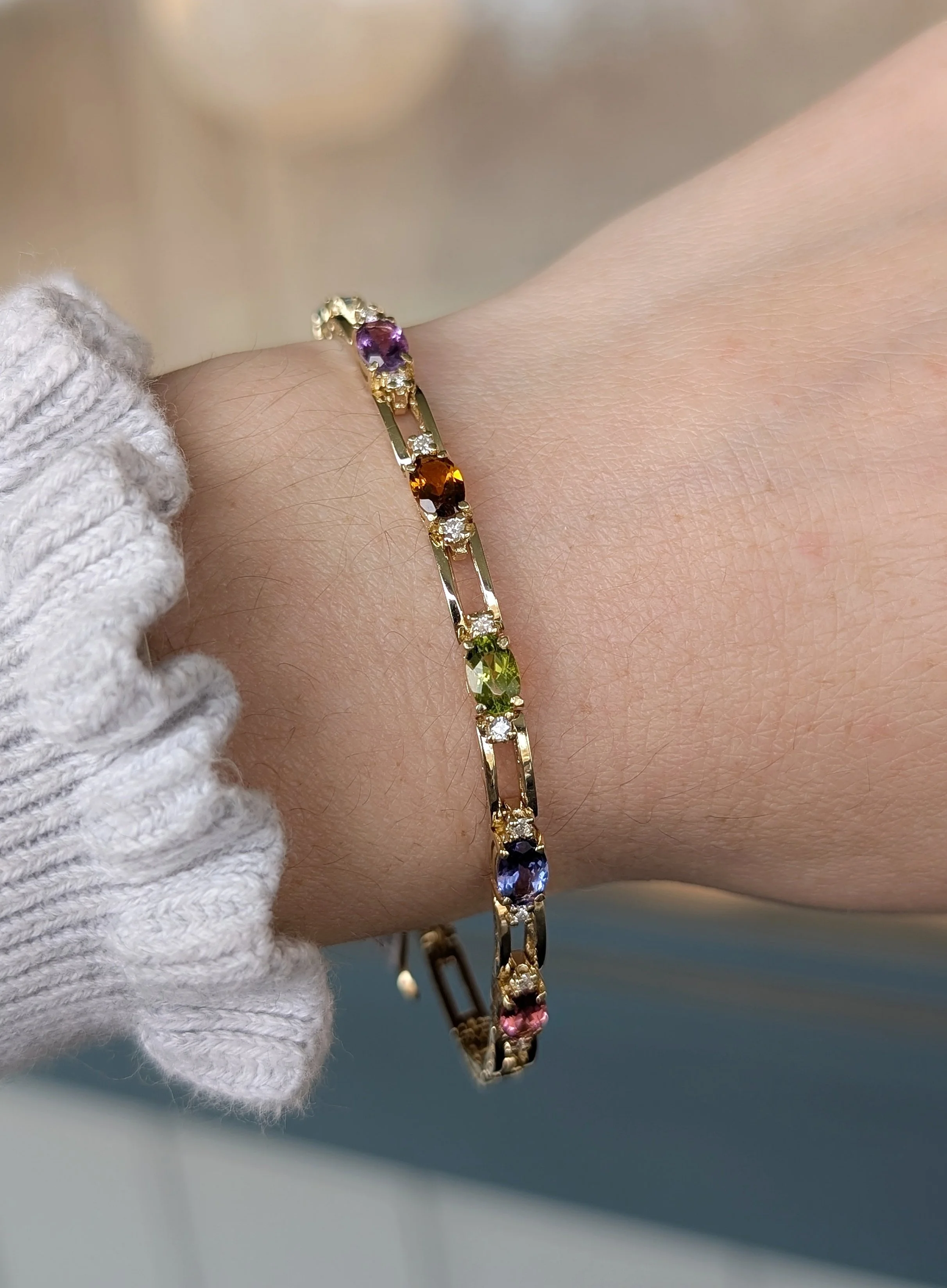 14k yellow gold mixed gemstone and diamond bracelet set with 1 garnet, 1 blue topaz, 1 amethyst, 1 citrine, 1 peridot, 1 tanzanite, and 1 pink tourmaline. (240-1177)