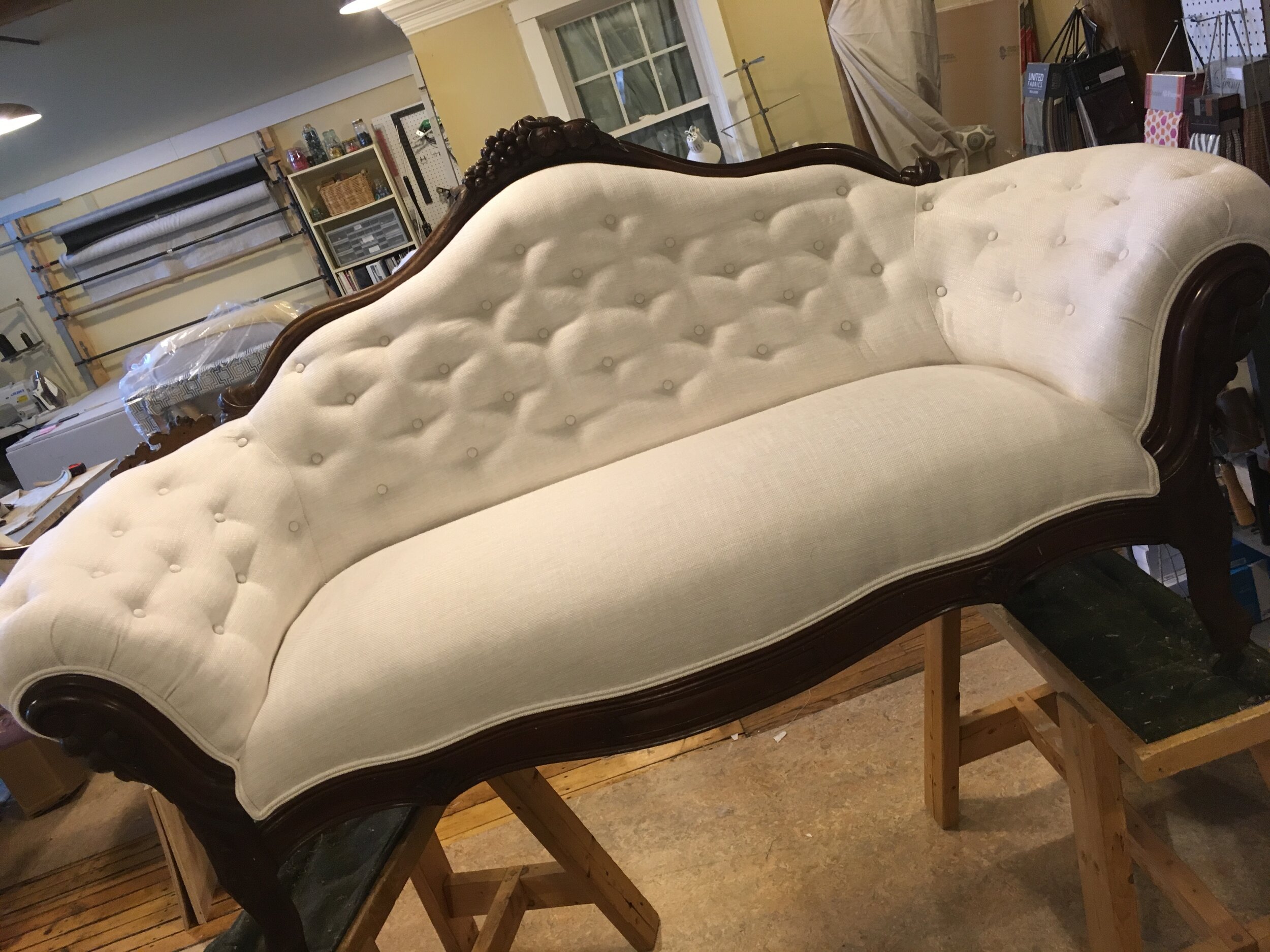 Antique white tufted sofa with wooden frame in workshop setting.