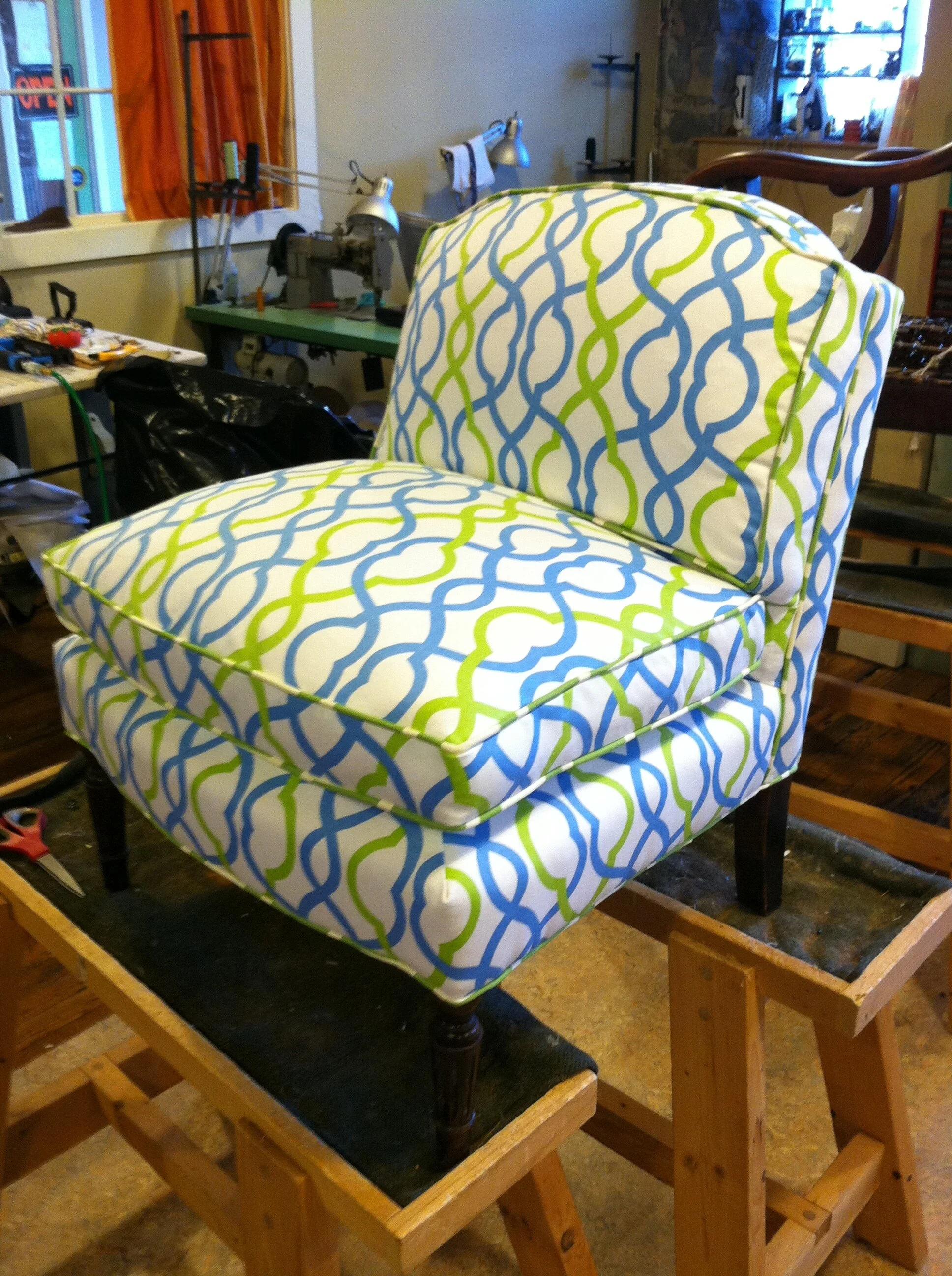 Patterned upholstered chair with blue and green interlocking design on a wooden frame, placed on a workbench.