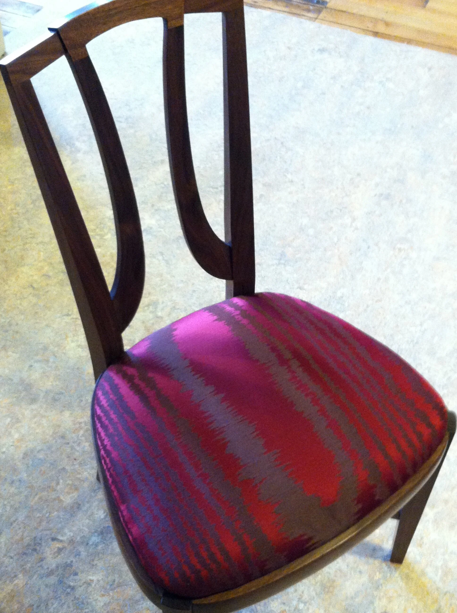 Wooden dining chair with a curved backrest and upholstered seat in red and purple pattern.