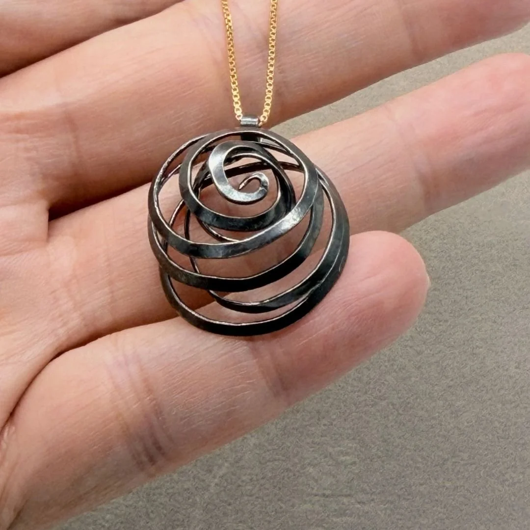 Freeform Spiral Necklace held in a hand, showing the scale of the one-inch oxidized sterling silver pendant.
