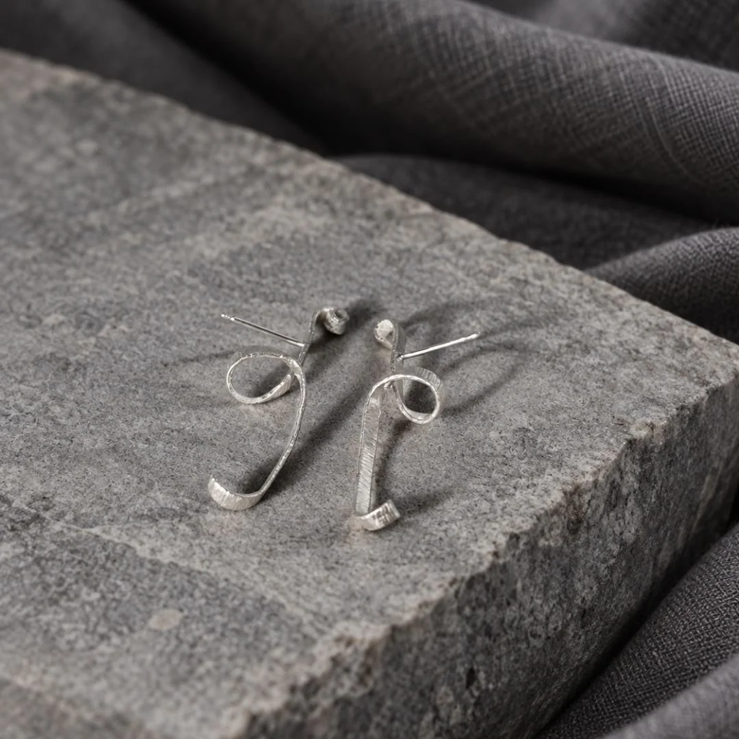 Side view of Unfolding Spiral sterling silver earrings, showing the posts and curled form on gray stone.