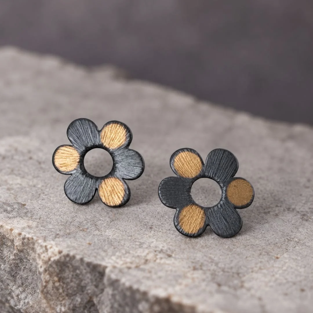 Front view of daisy-shaped earrings showing lightly textured petals in dark silver and gold.
