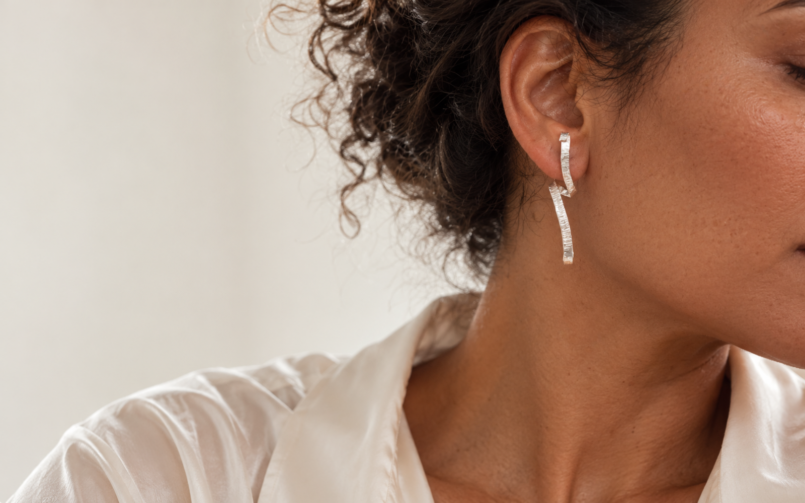 Model wearing a textured sterling silver Unfolding Spiral earring with an off-white shirt.