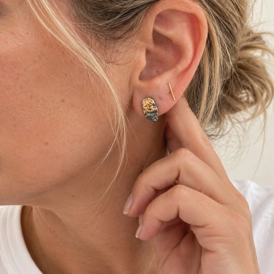 Close-up of a woman wearing a petite textured oval stud earring with gold accents, her hand resting near her ear.