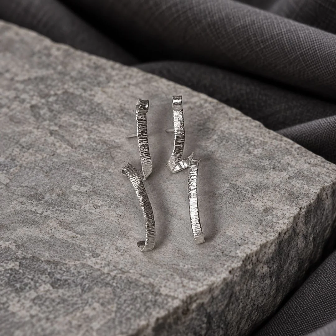 Front view of textured sterling silver spiral earrings standing on gray stone.