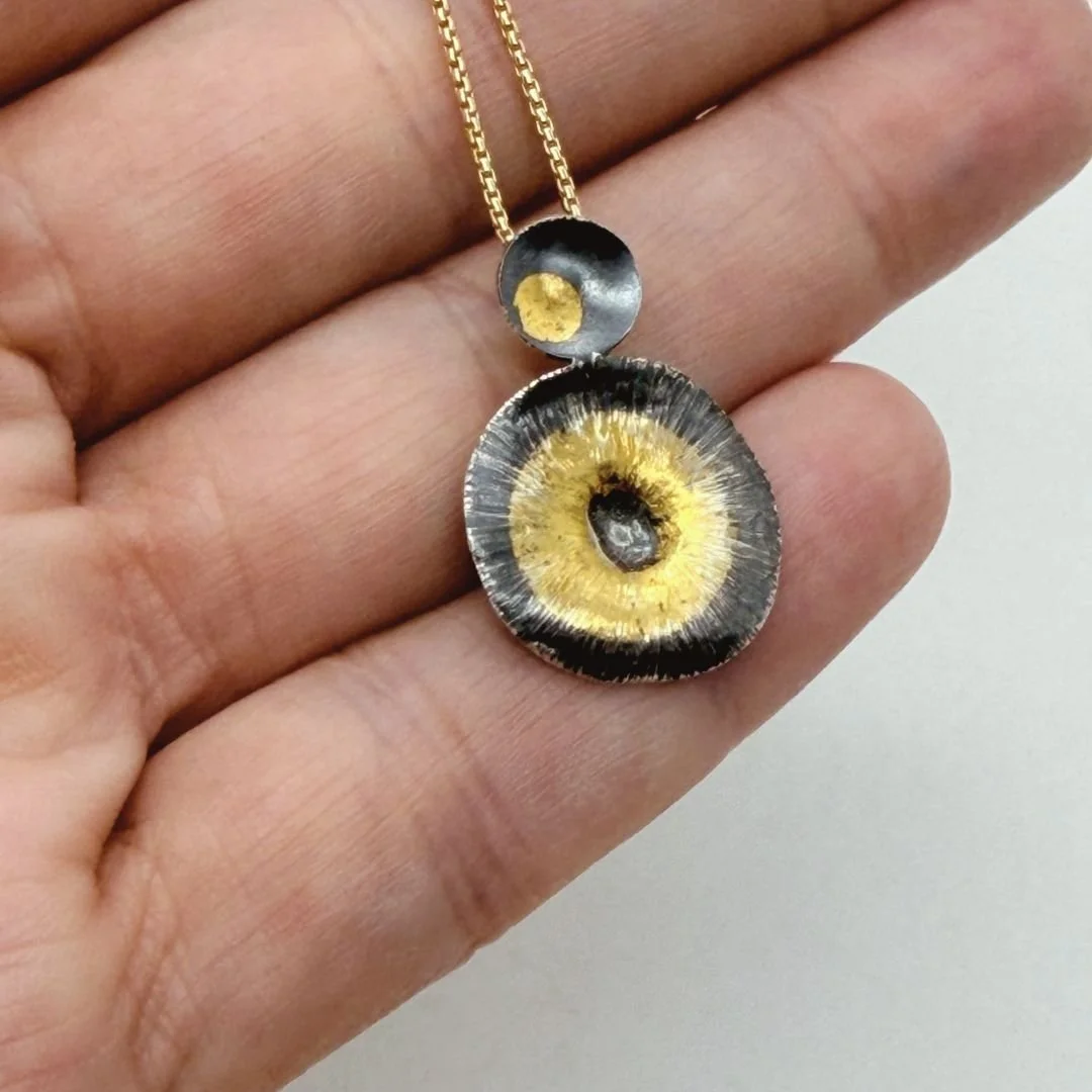 Echo mixed metal pendant in oxidized sterling silver and gold on a hand for scale