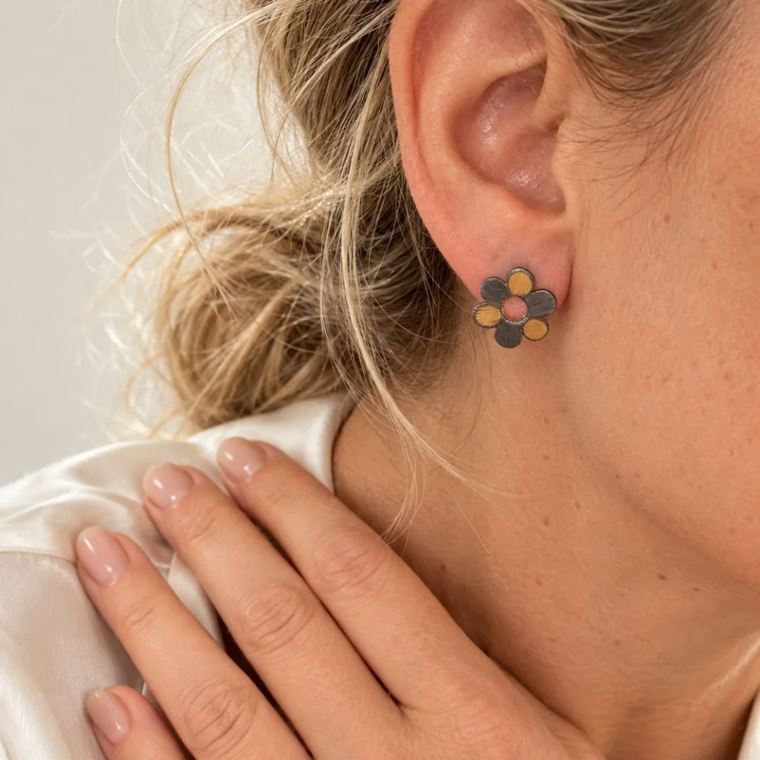 Woman wearing a black and gold flower stud earring, showing its size on the ear.