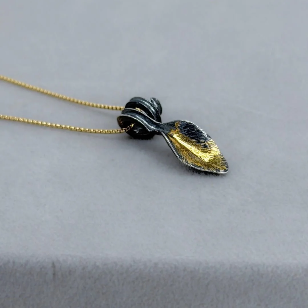Close-up of Autumn Leaf pendant in oxidized sterling silver and gold resting on a gray surface