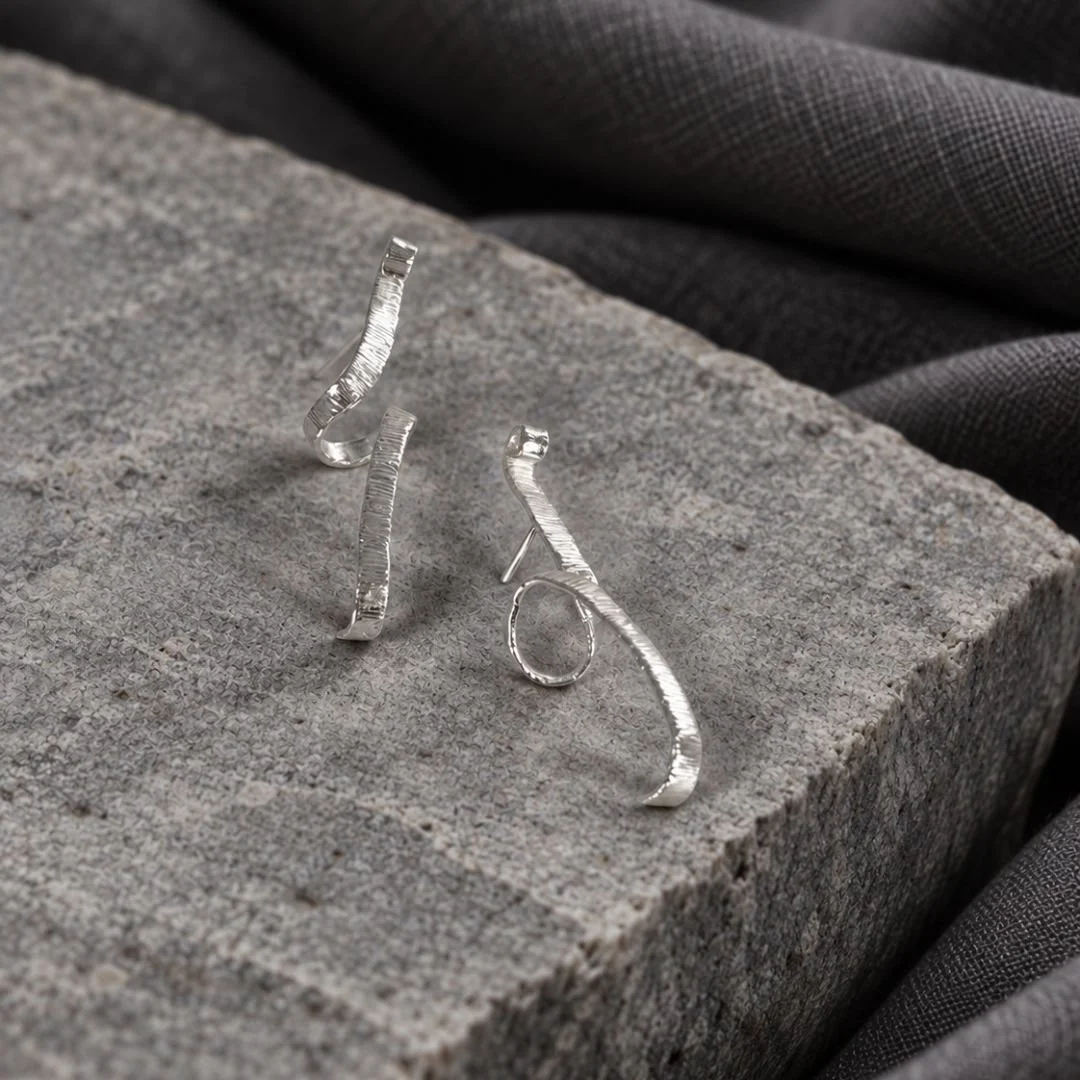 Angled view of Unfolding Spiral earrings showing their textured silver surface and open curves.