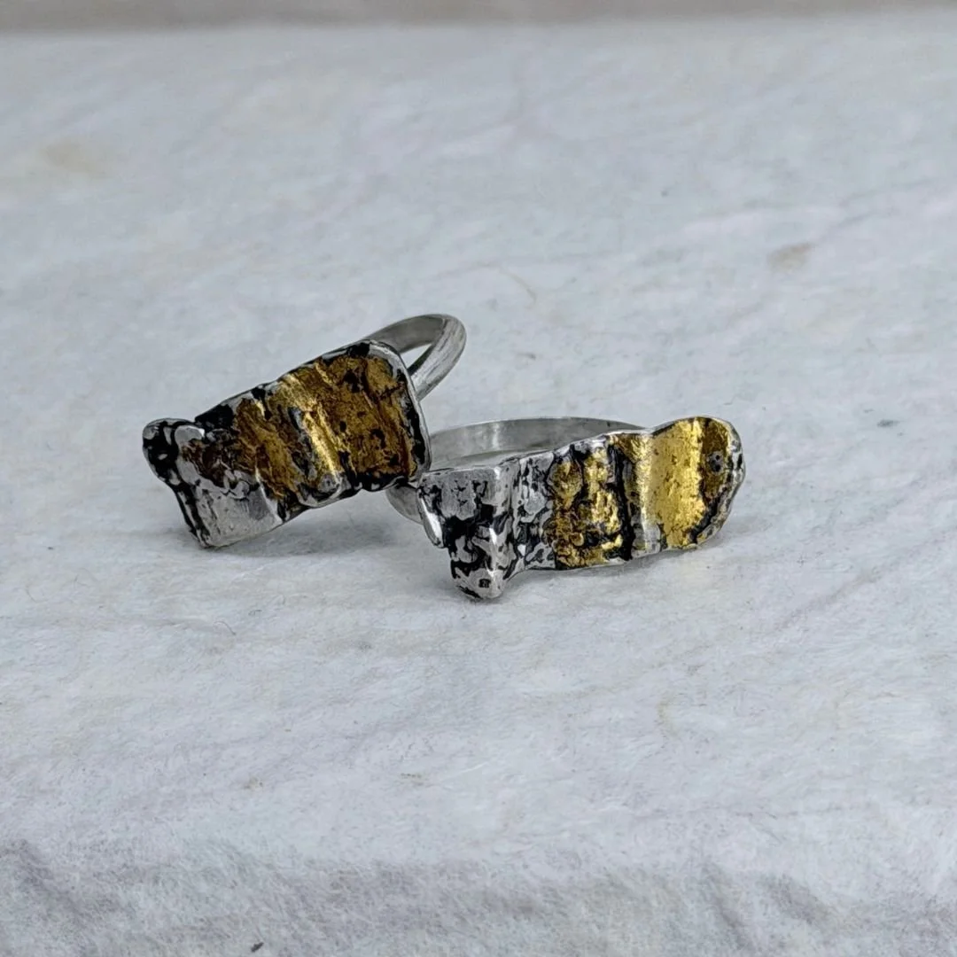 Two Petite Textured silver and gold rings on a gray surface, showing their different textures and keum-boo gold placement