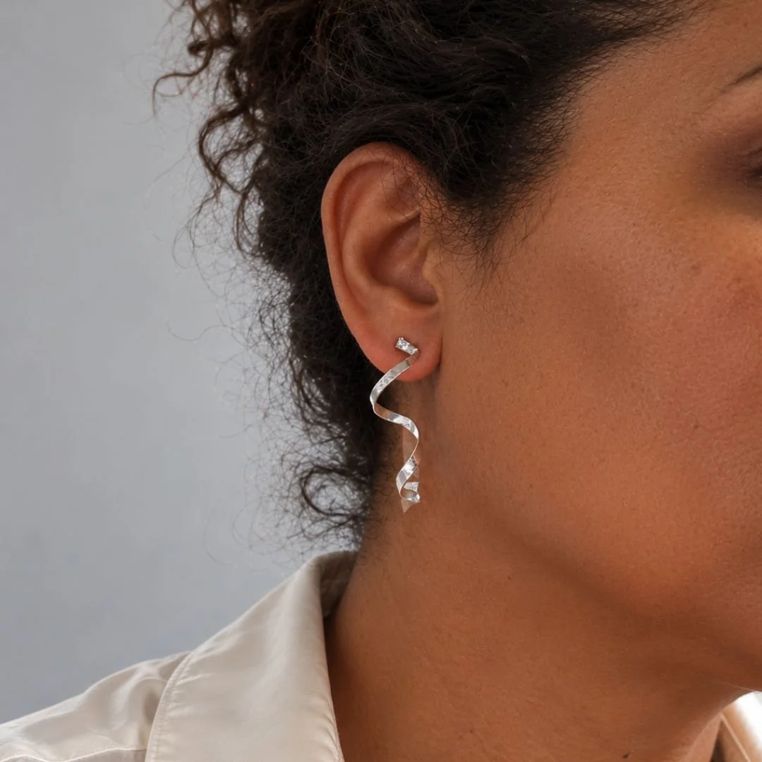 Spiral Ribbon earring worn on the ear, showing its 1.5-inch length and textured matte silver finish.