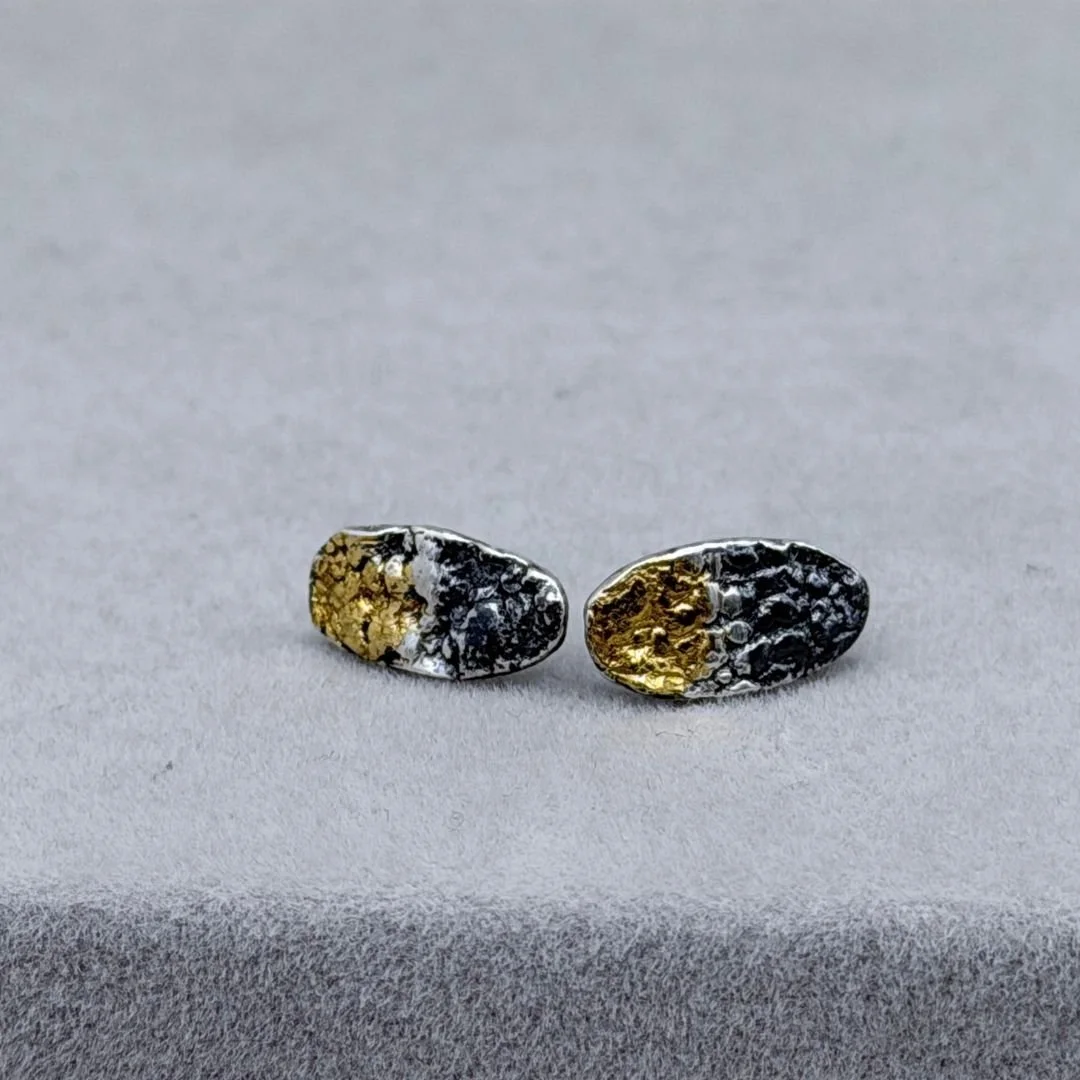 Textured oval stud earrings in oxidized sterling silver with 23.5k keum-boo gold on a gray background