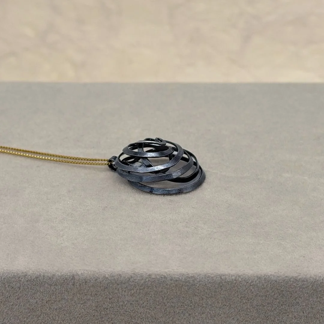 Side view of the Freeform Spiral Necklace on a gray surface, showing the raised curves of the silver pendant.