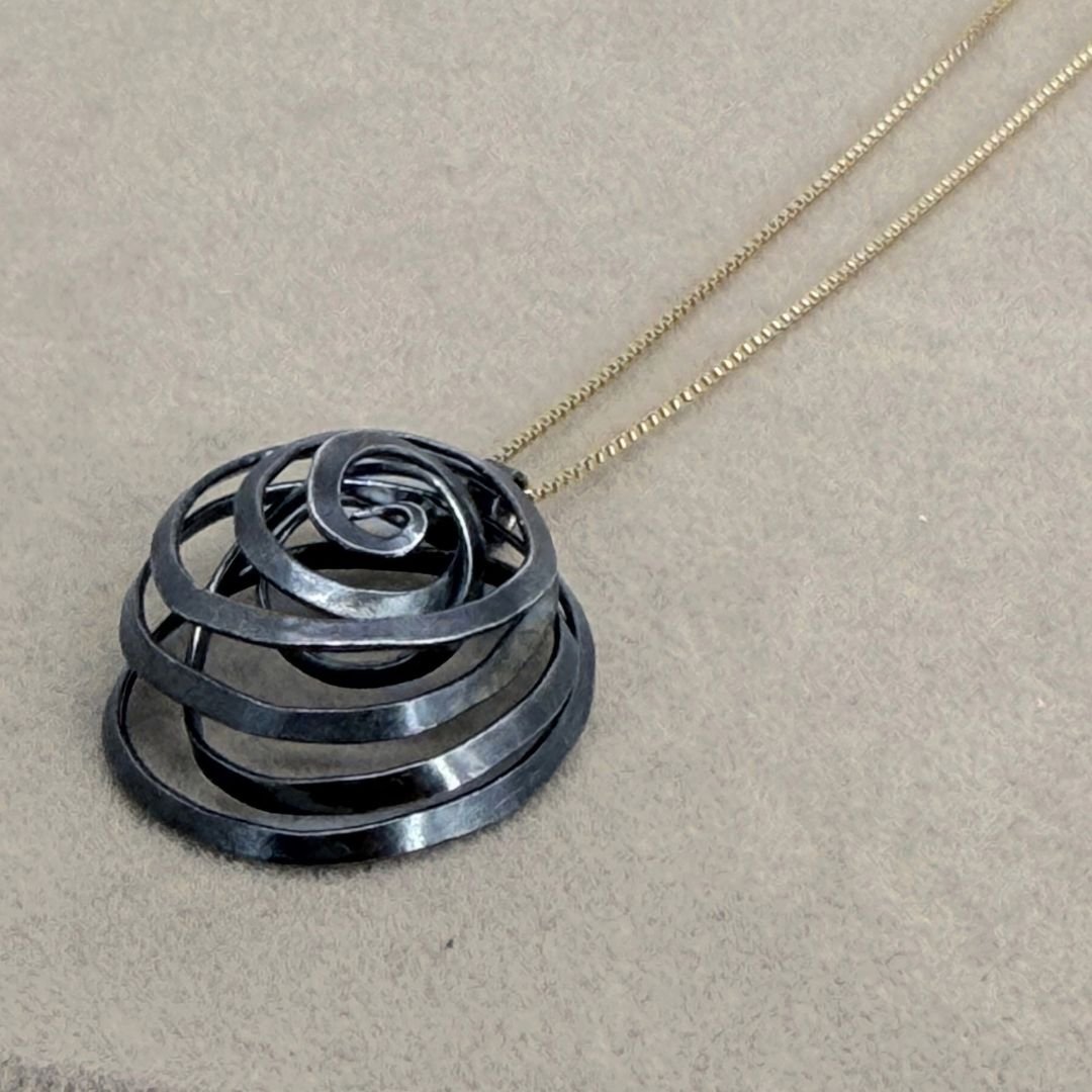 Close-up of the Freeform Spiral Necklace, showing its dark silver finish and gold-filled chain on a gray surface.