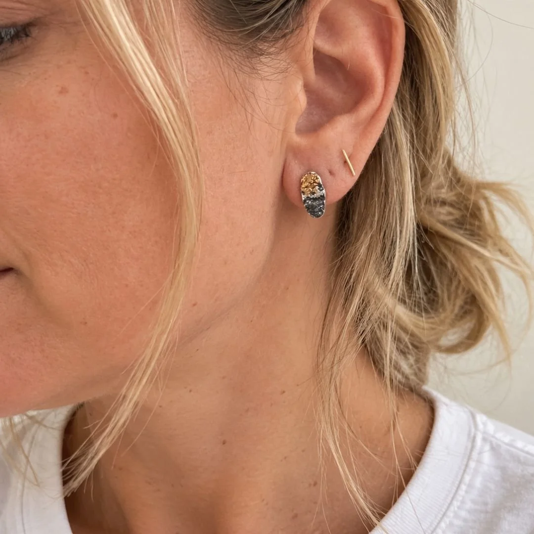 Petite oxidized silver and gold oval stud earring worn by a woman in a white shirt