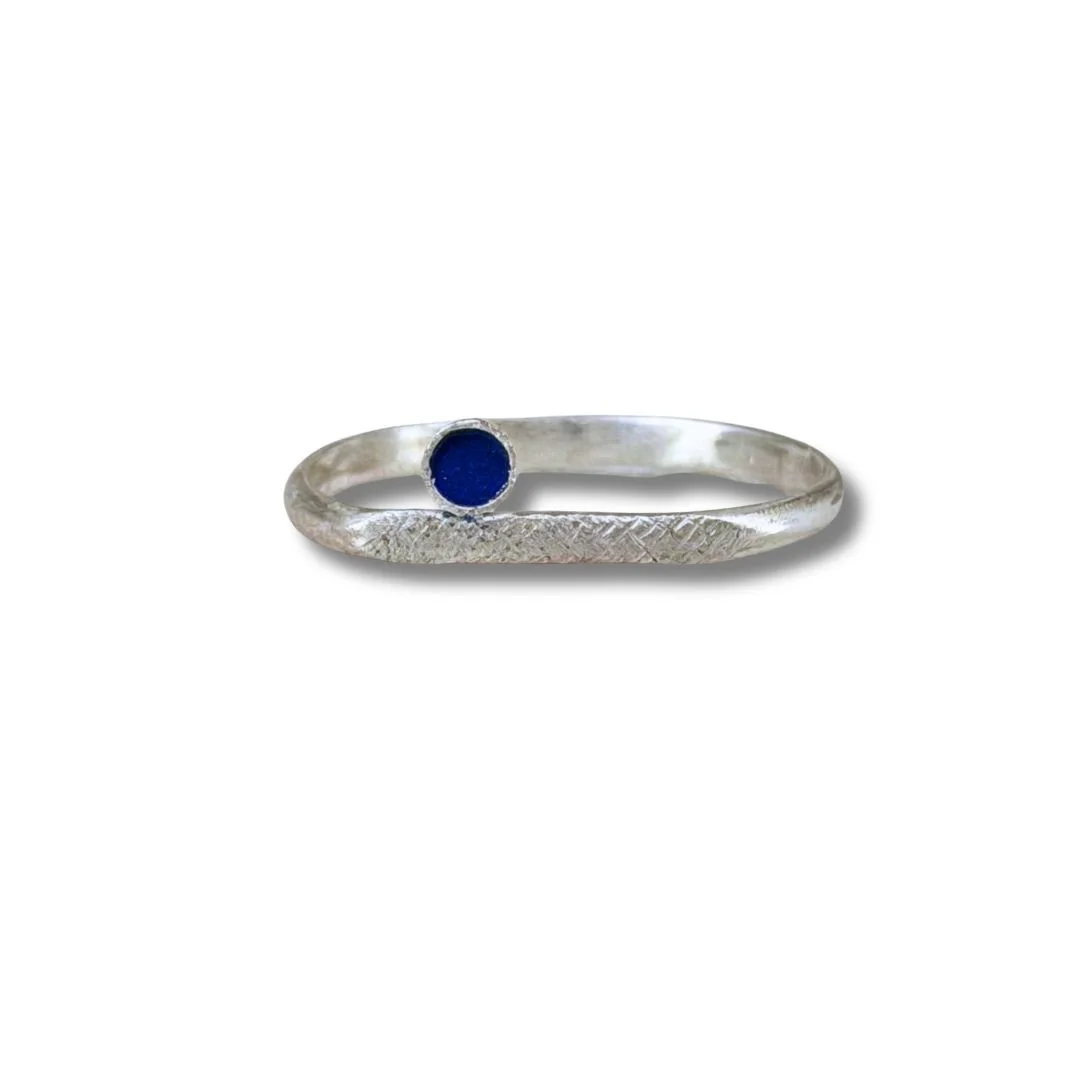 Sterling silver stacking ring with a deep blue enamel dot on a textured band.