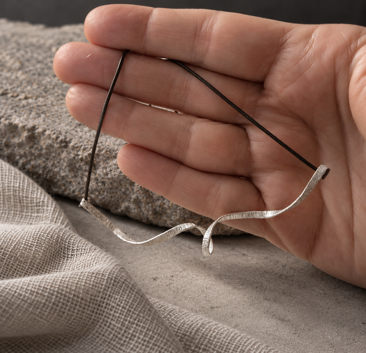 Spiral Unfolded Necklace held against a hand, showing the scale and texture of its silver centerpiece.