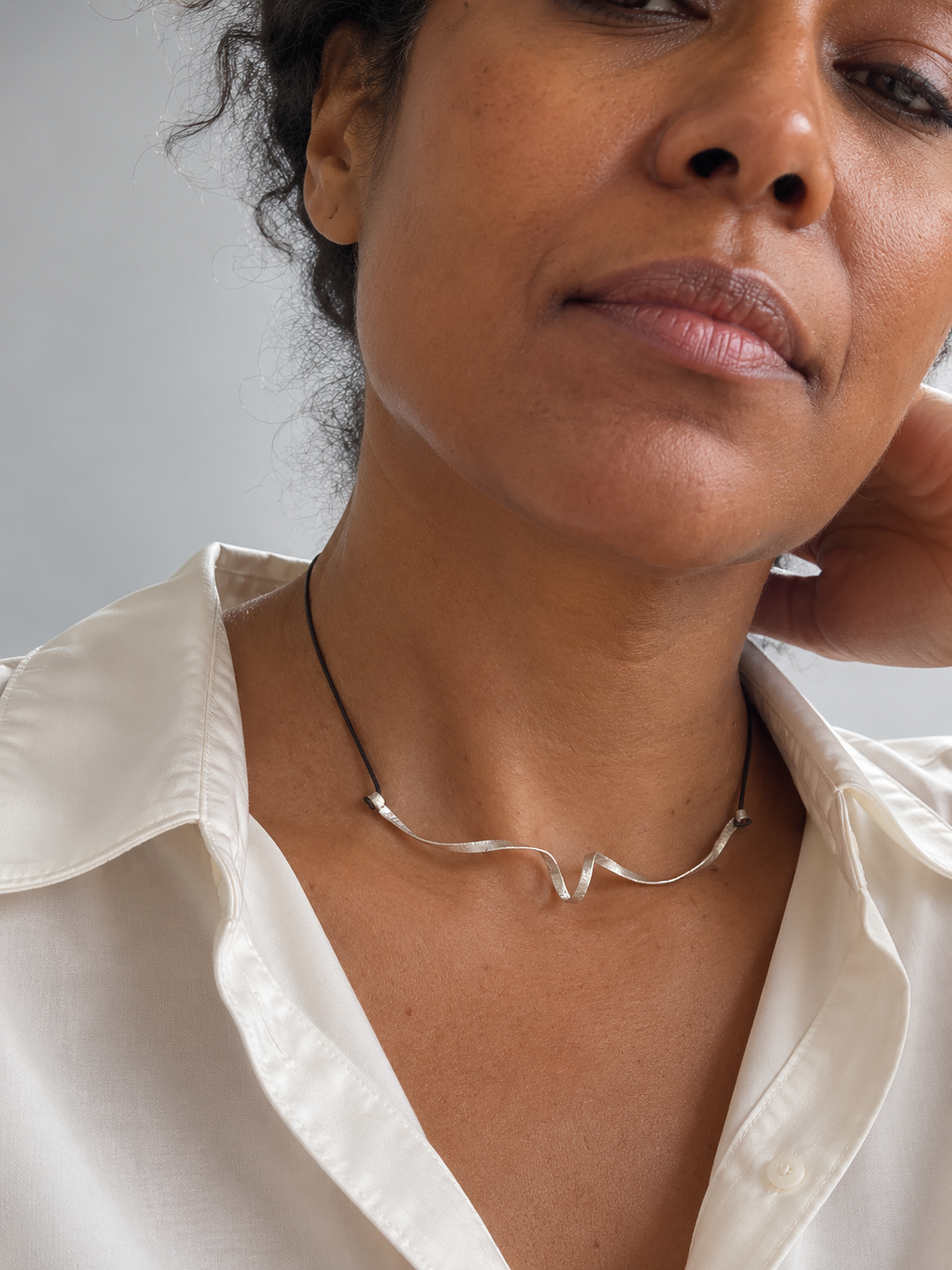 Spiral Unfolded Necklace worn with an open-collar white shirt, showing how the curved silver form sits across the neckline.