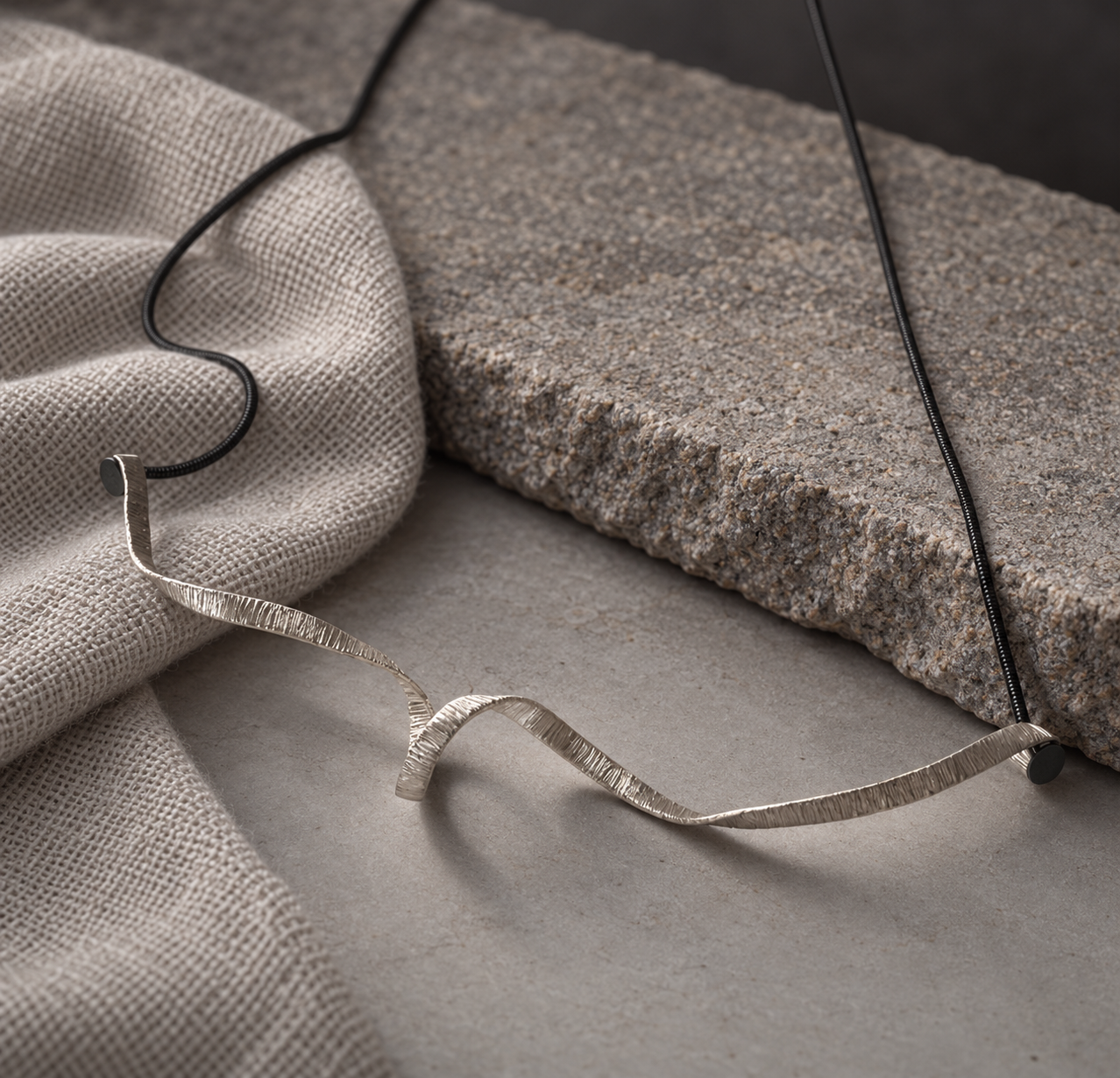 Angled view of the textured silver centerpiece, showing its unfolding curves on gray stone beside woven fabric.