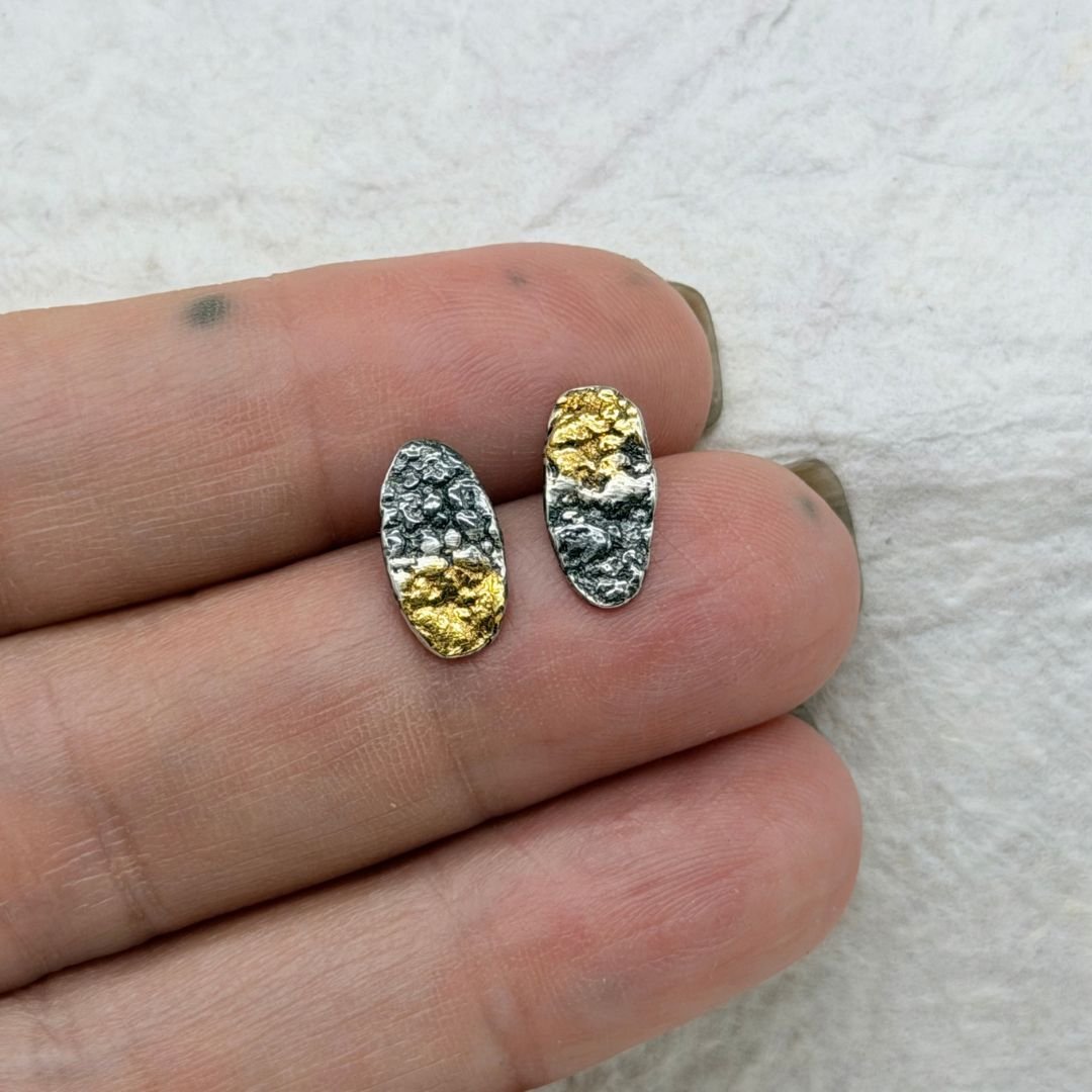 Petite Oval stud earrings held in a hand to show their half-inch size and textured silver and gold finish