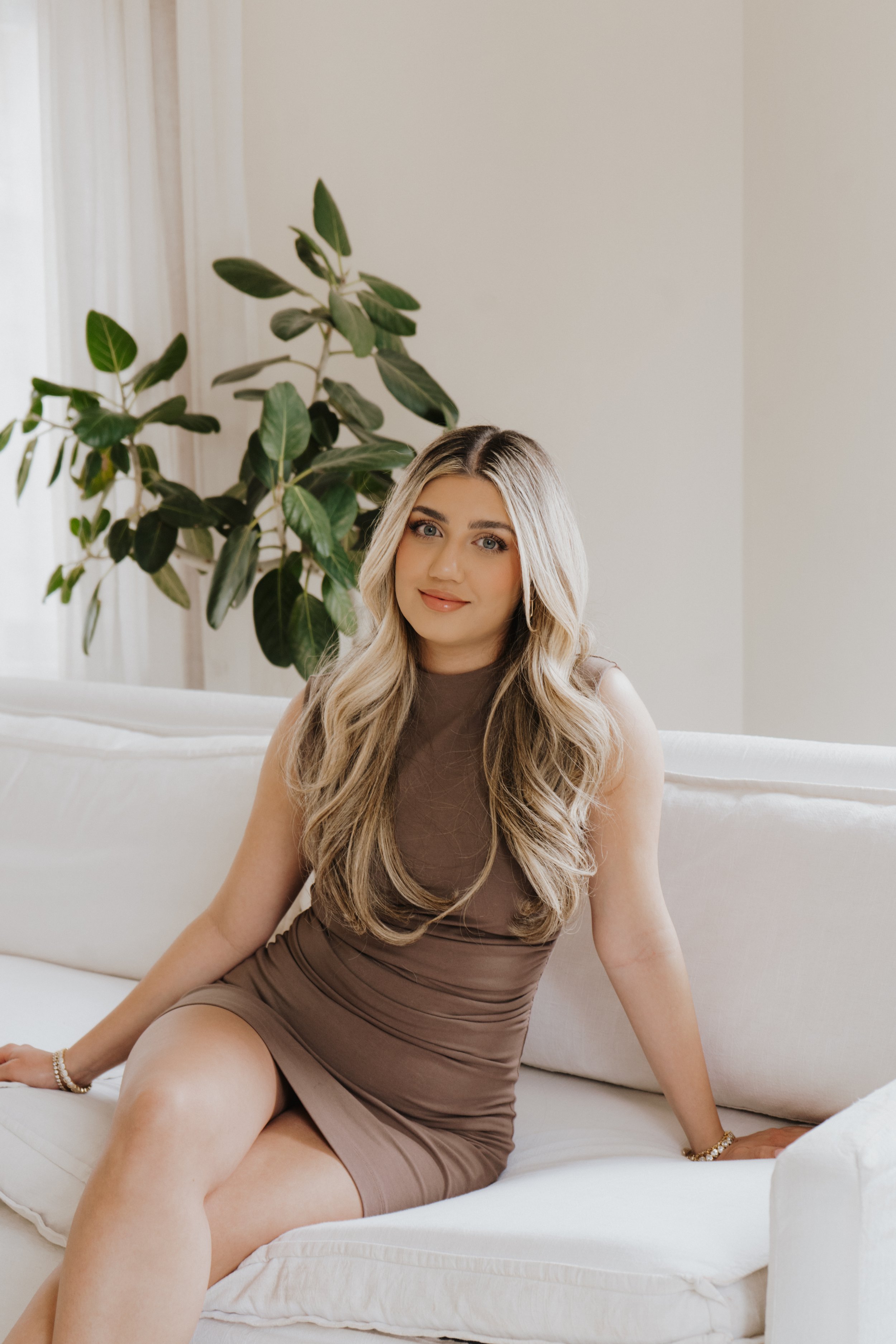 Woman sitting on a white couch with a plant in the background