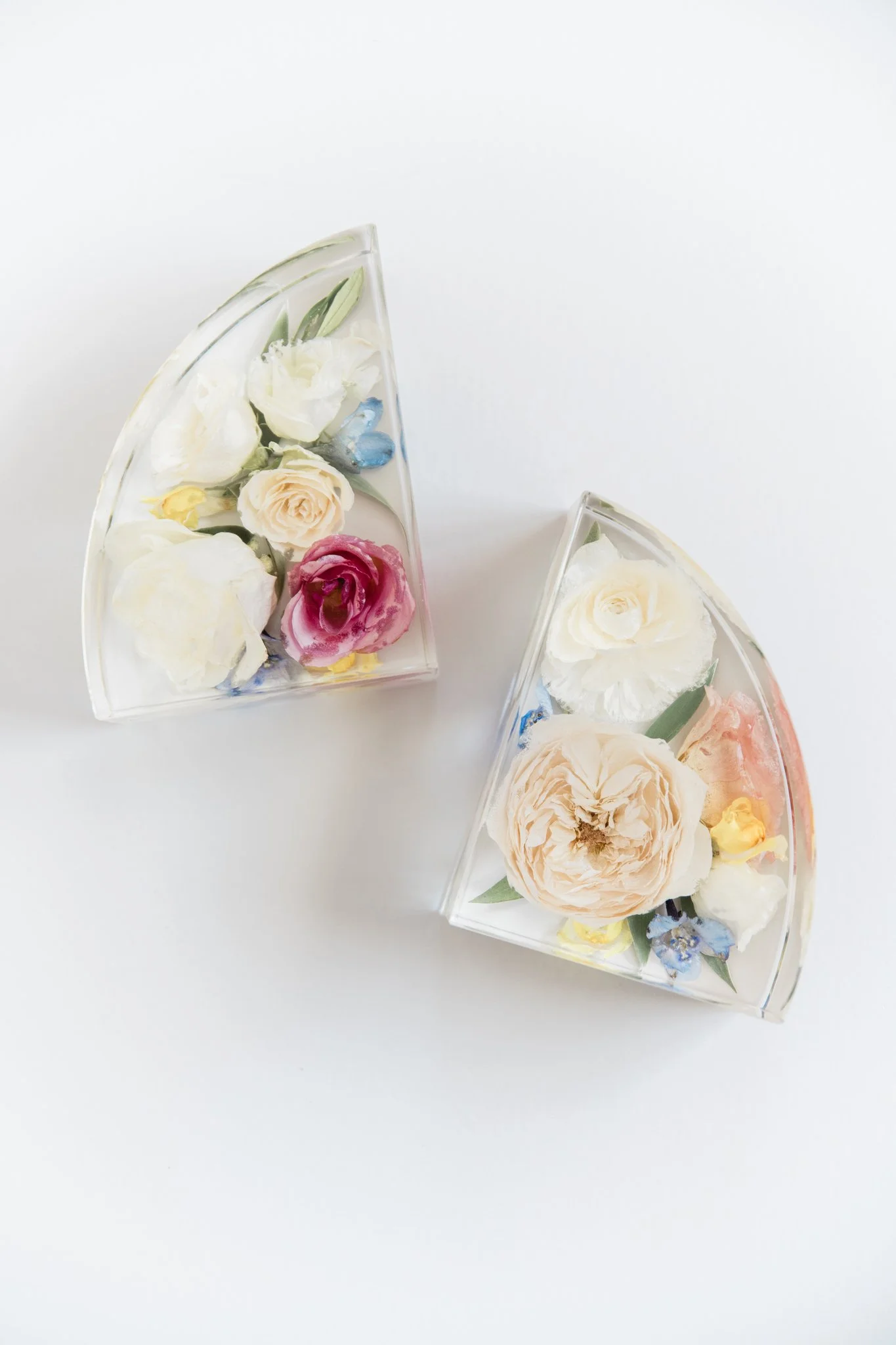 Two transparent glass bowls shaped like cake slices filled with white and pink flowers, on a white background.