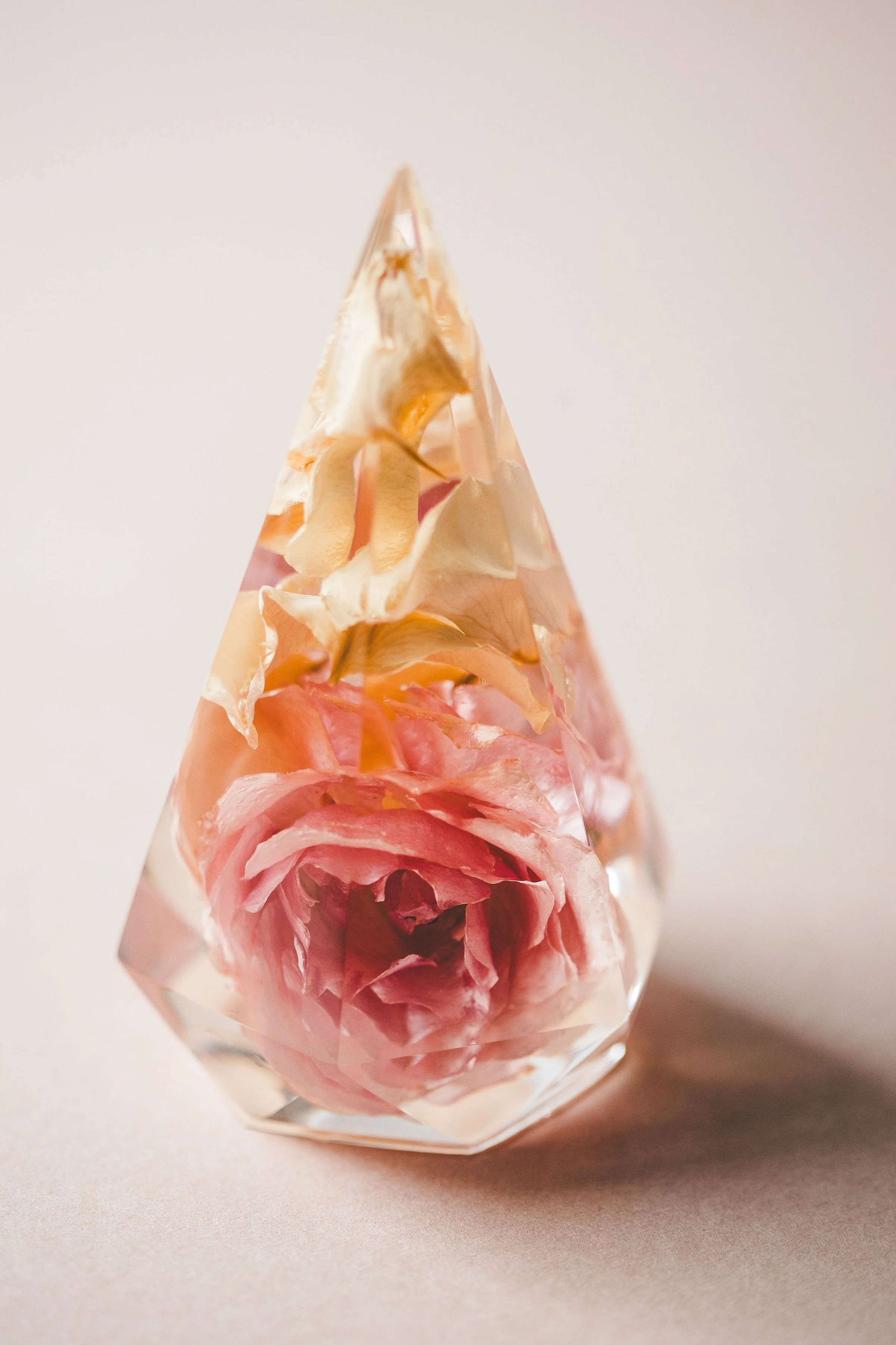 A glass pyramid with a pink rose flower inside, creating a decorative display.