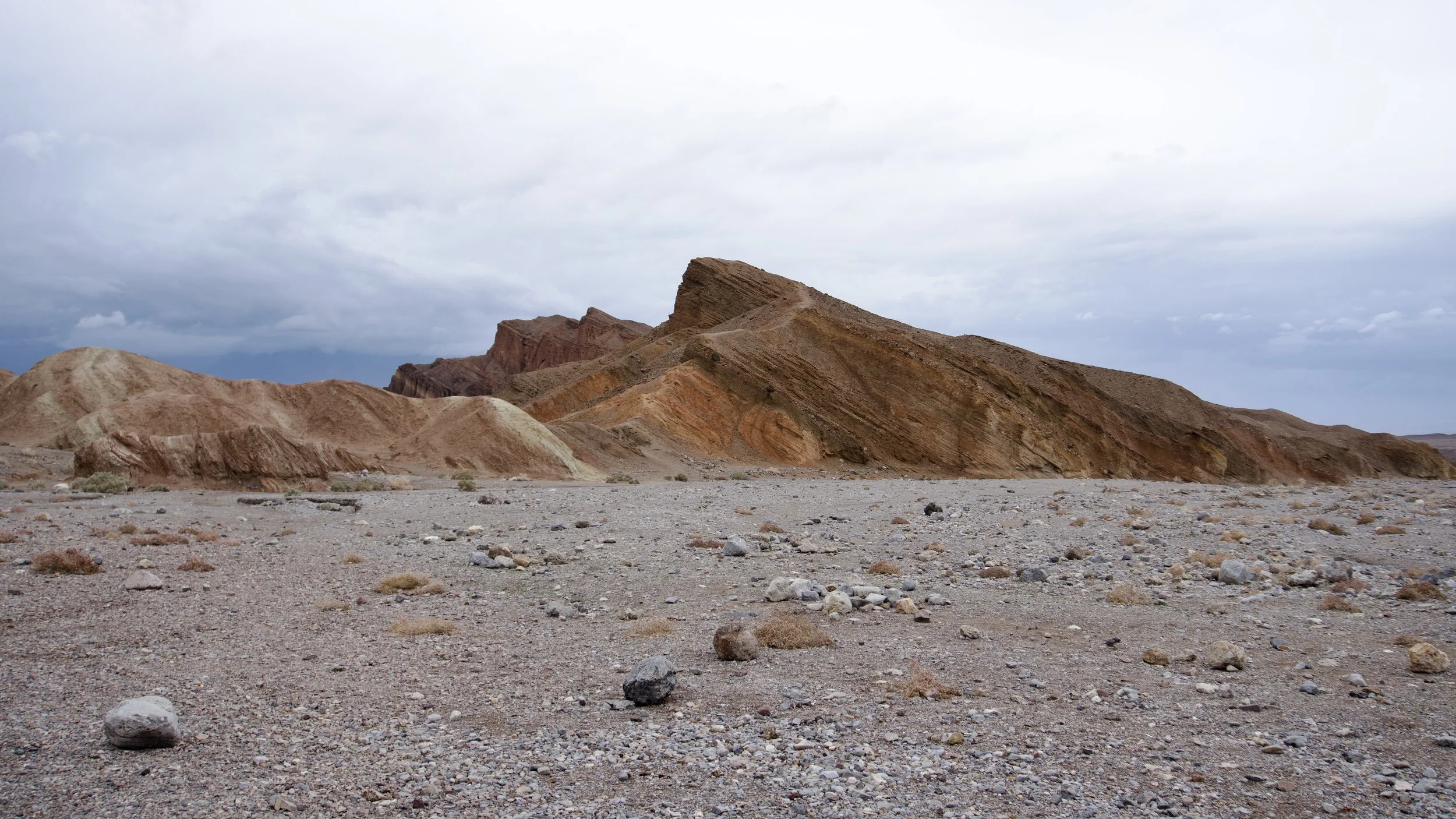 Desert landscape with colorful, layered mountains under an overcast sky.