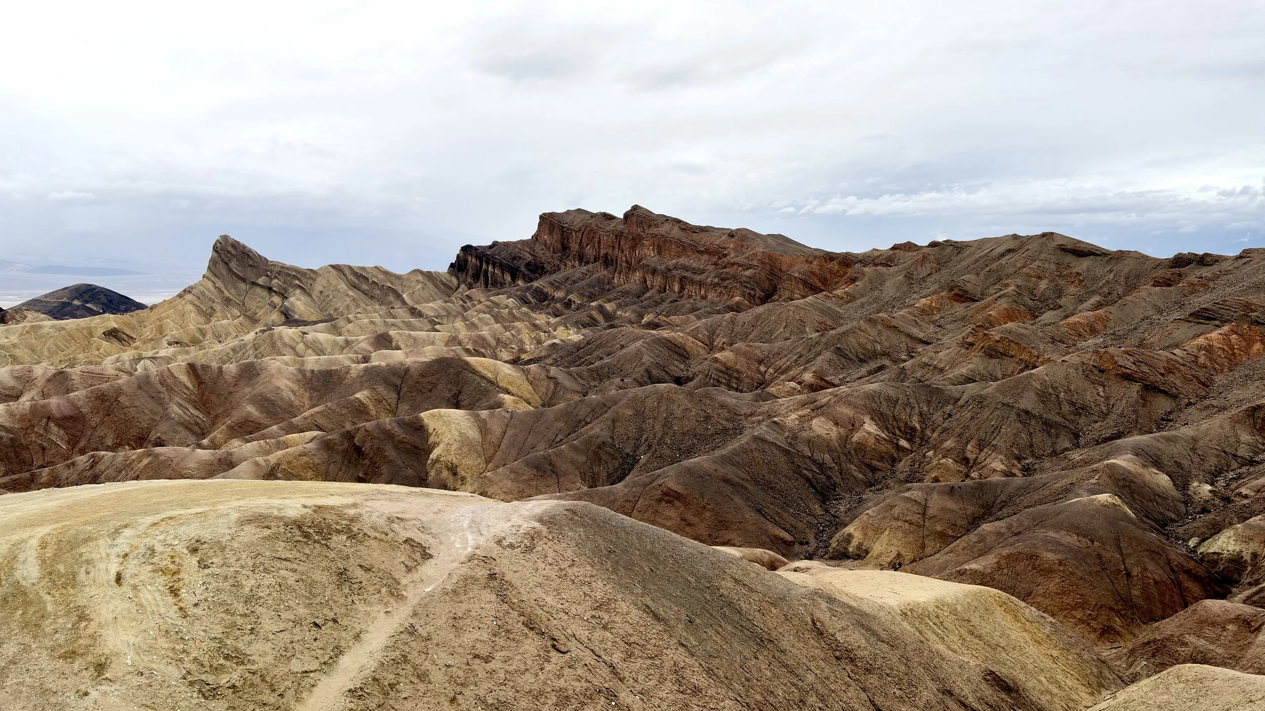 Colorful, layered hills and mountains under a cloudy sky in a remote desert landscape.