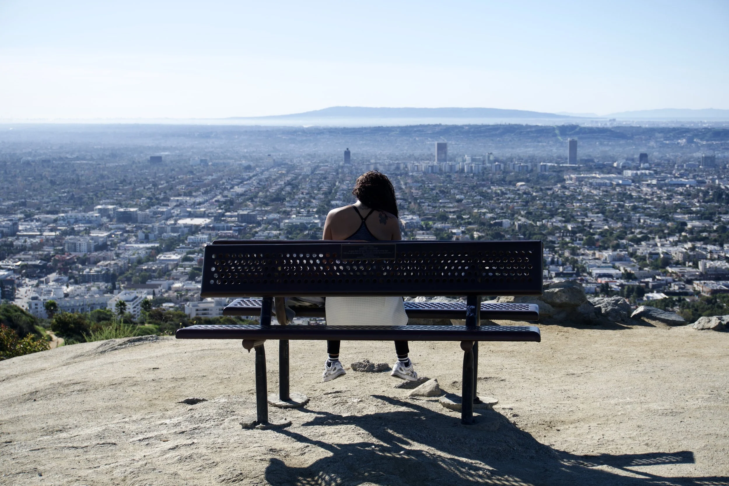 Person sitting on a bench overlooking a cityscape from a hilltop