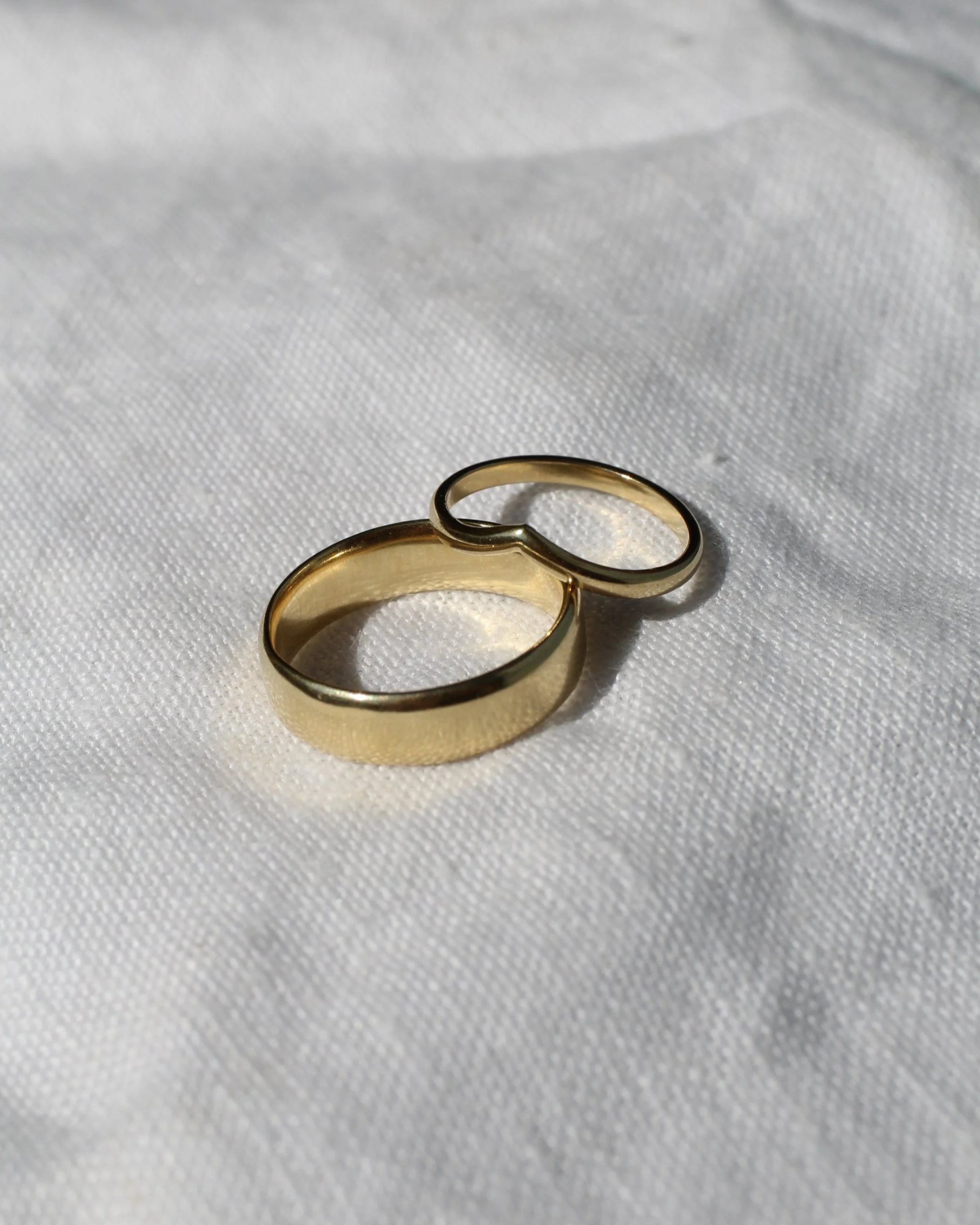 Two gold wedding bands resting on a white textured fabric surface.