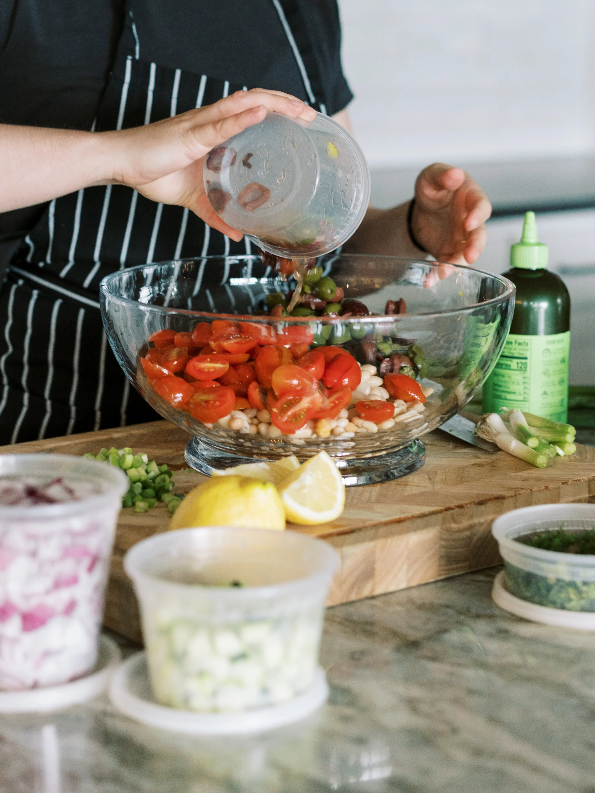 Chef preparing a colorful fresh salad with tomatoes, beans, herbs, and seasonal ingredients.