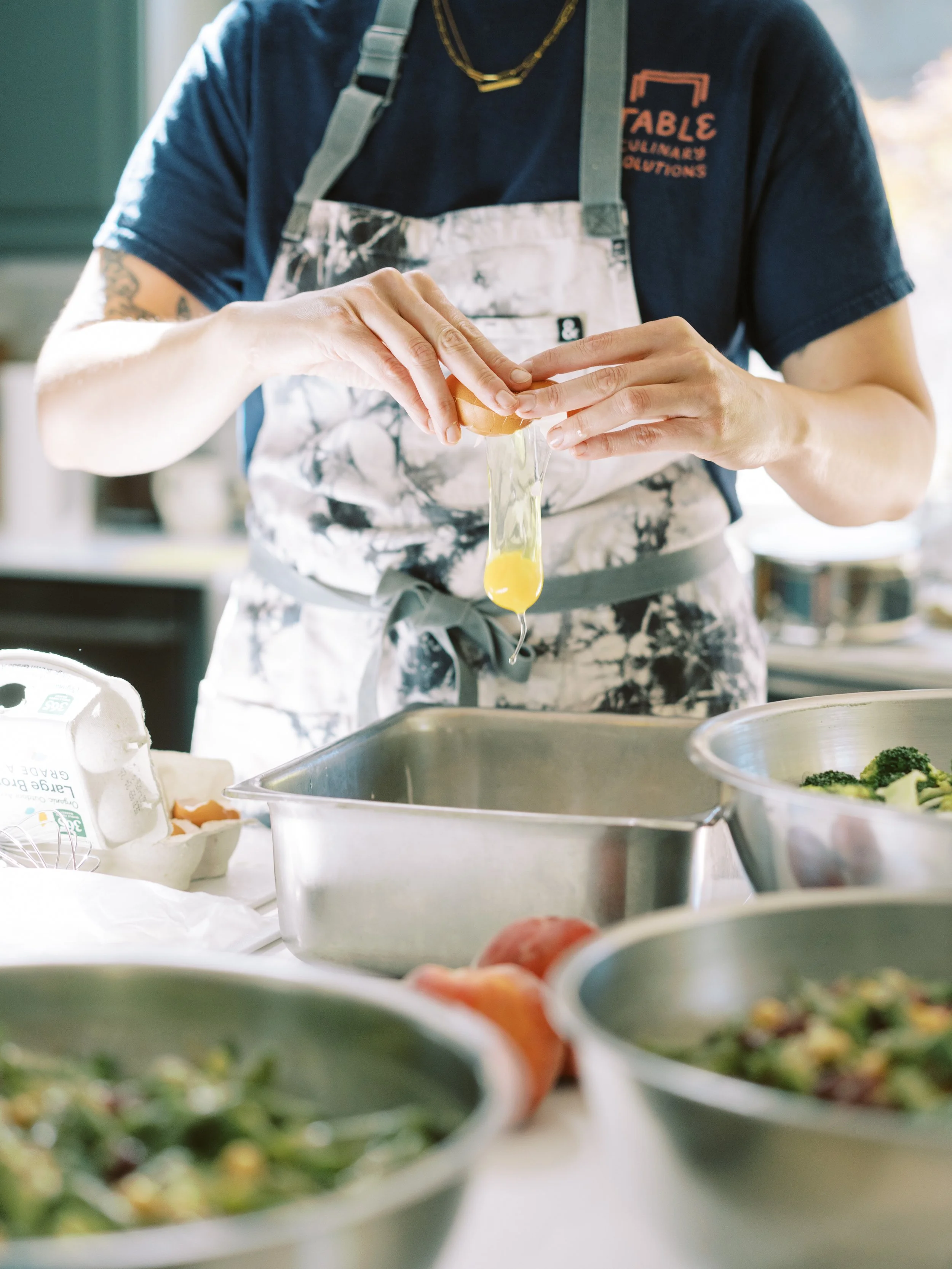 Private chef cracking an egg while preparing a freshly made meal in a home kitchen.